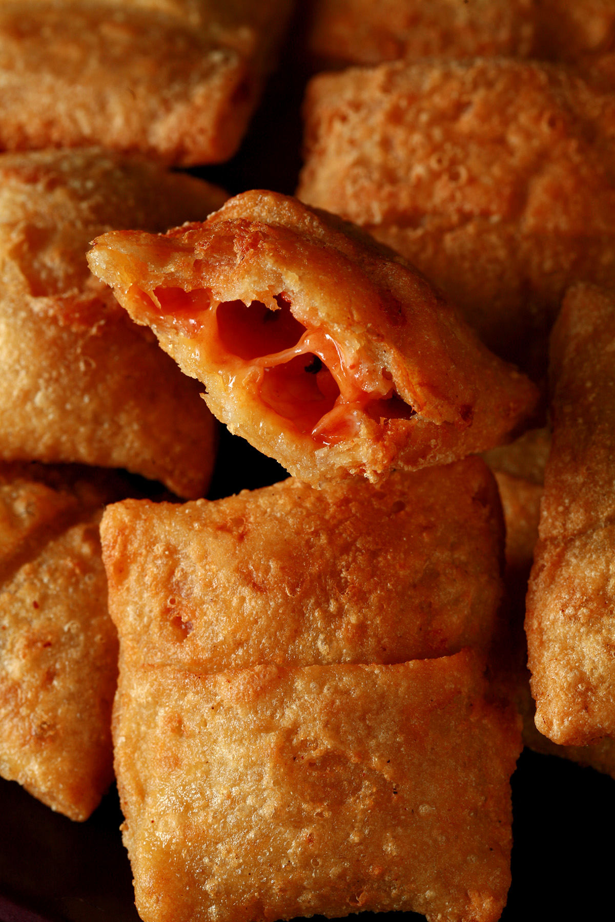 A plate with a pile of gluten-free pizza bites. One has been cut in half to show its pizza filling.