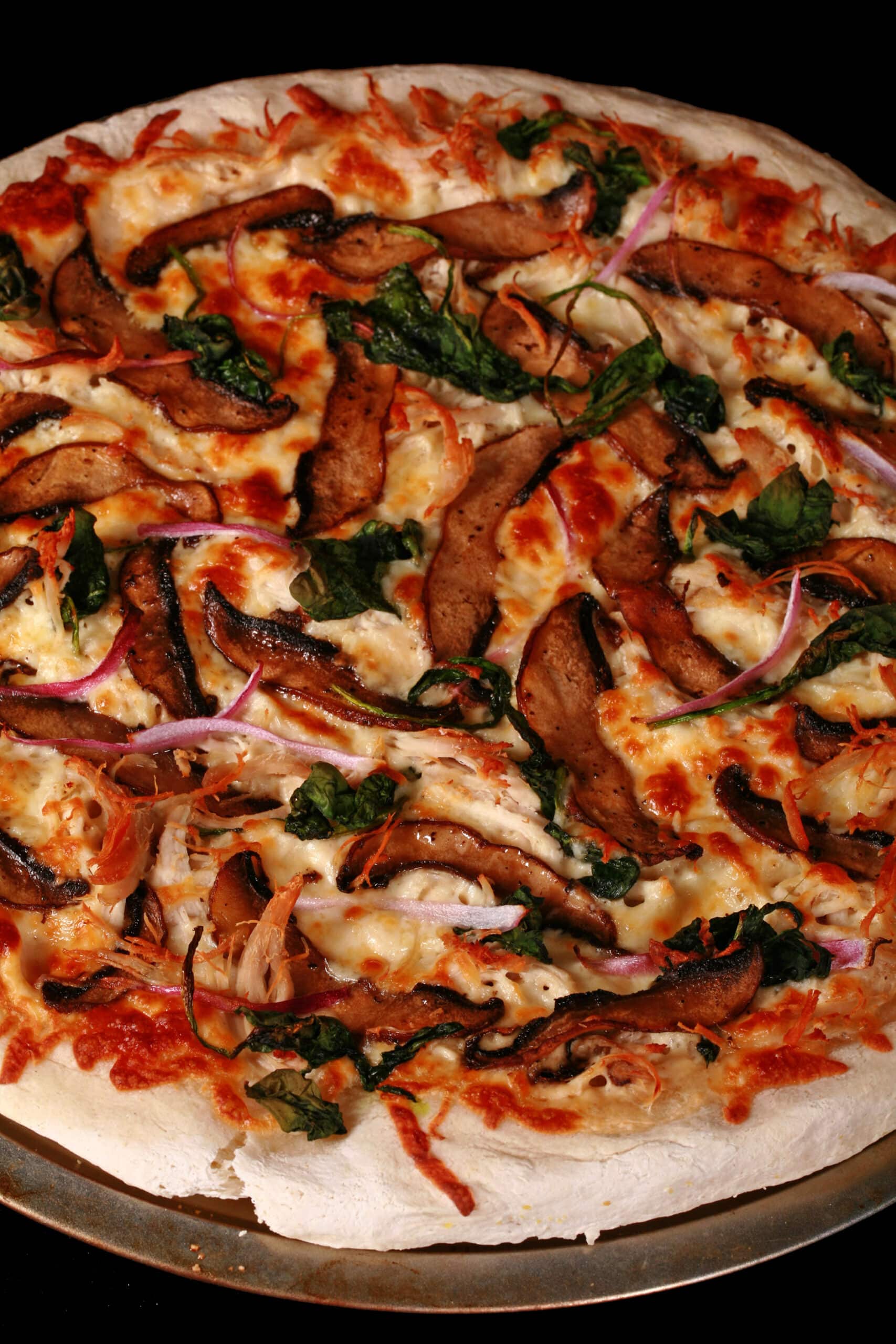 A gluten free pizza with mushrooms, spinach, and onions showing.