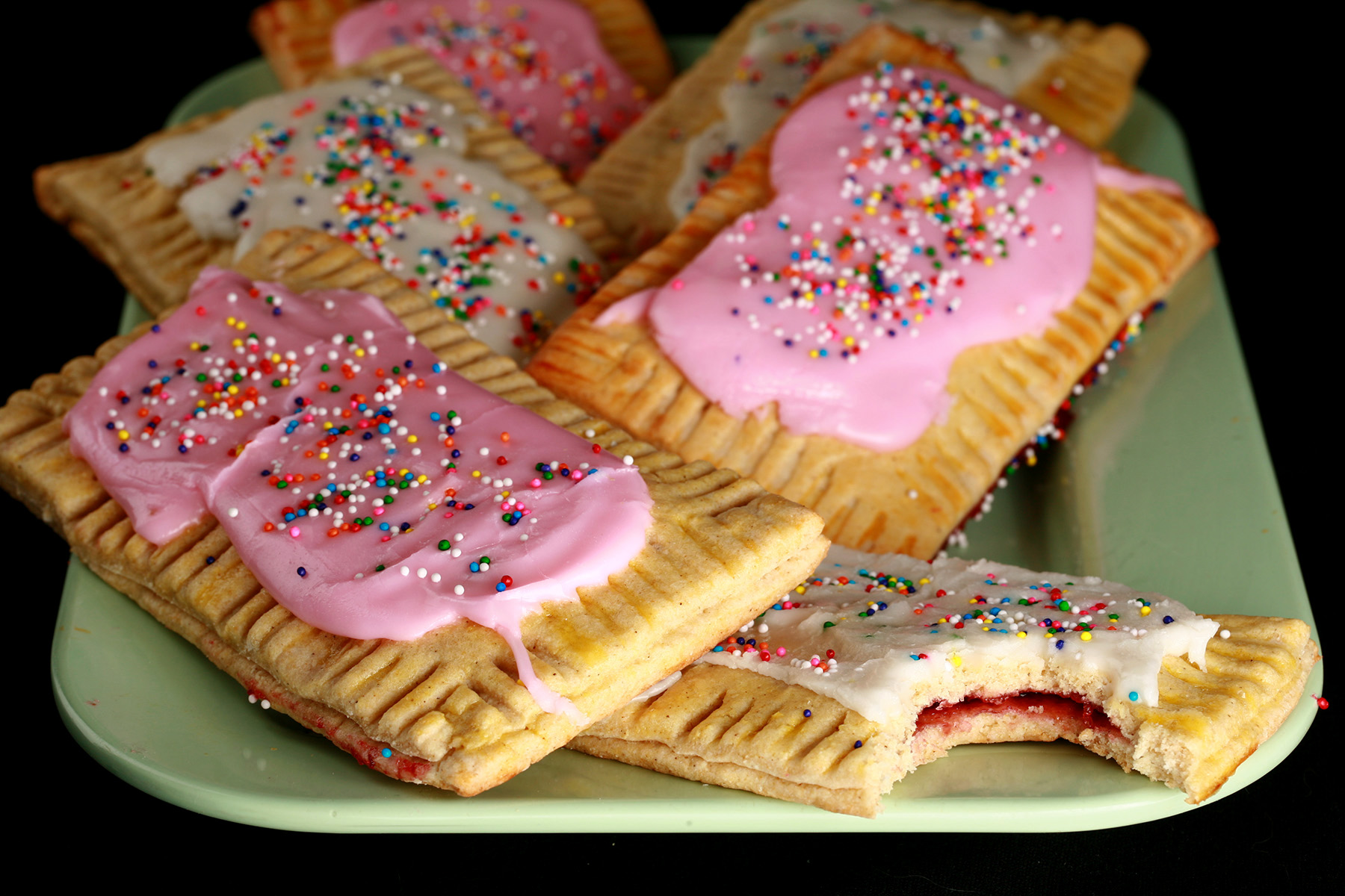 A plate of toaster pastries made from this gluten-free poptarts recipe. They are frosted with pink and white icing, and topped with coloured sprinkles.