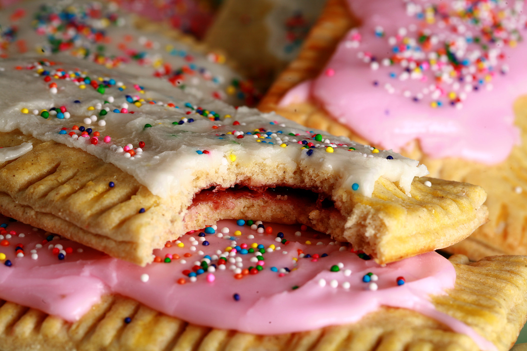 A plate of homemade gluten-free pop tarts, frosted with pink and white icing, topped with coloured sprinkles.