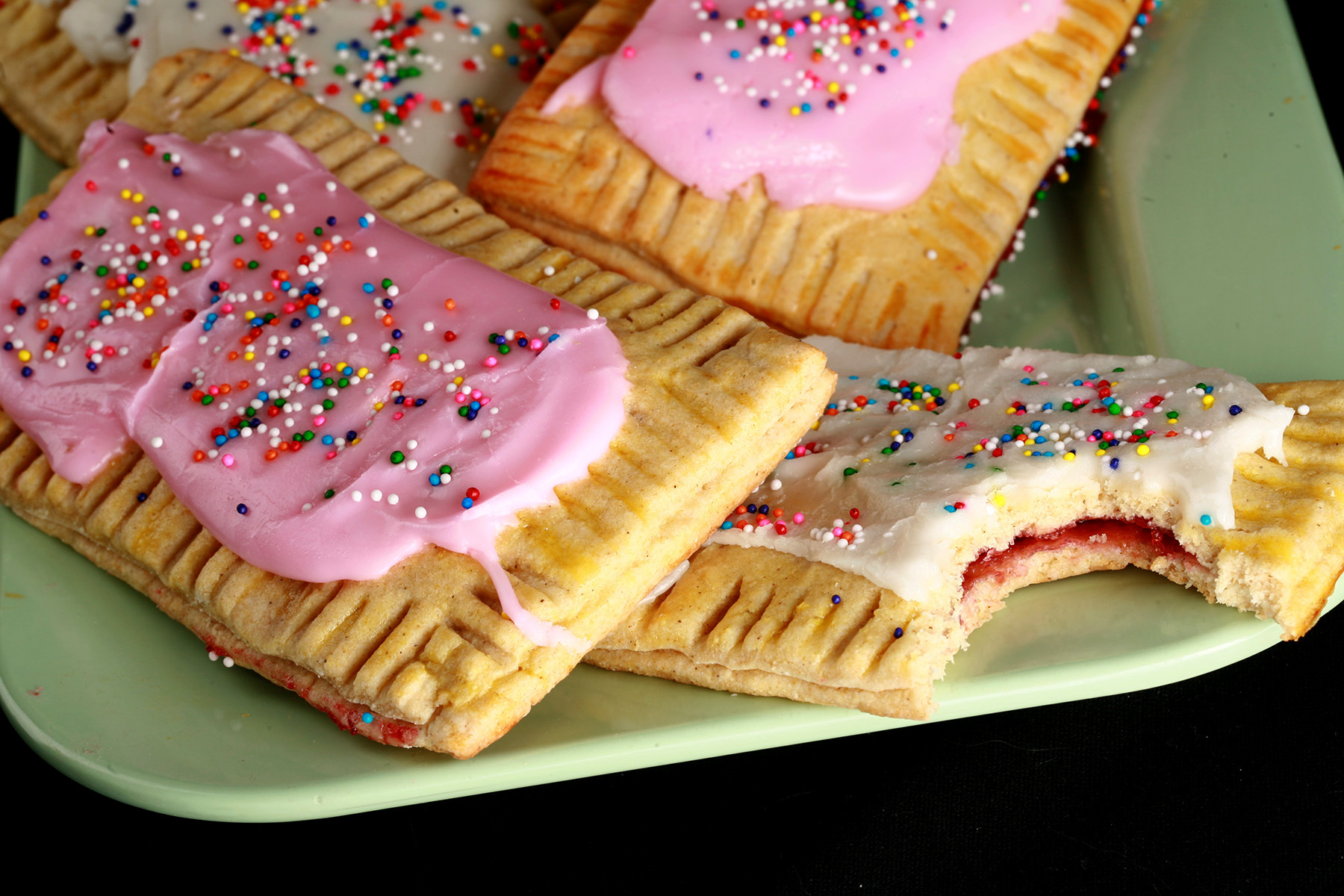 A plate of gluten free homemade poptarts, frosted with pink and white icing, topped with coloured sprinkles.