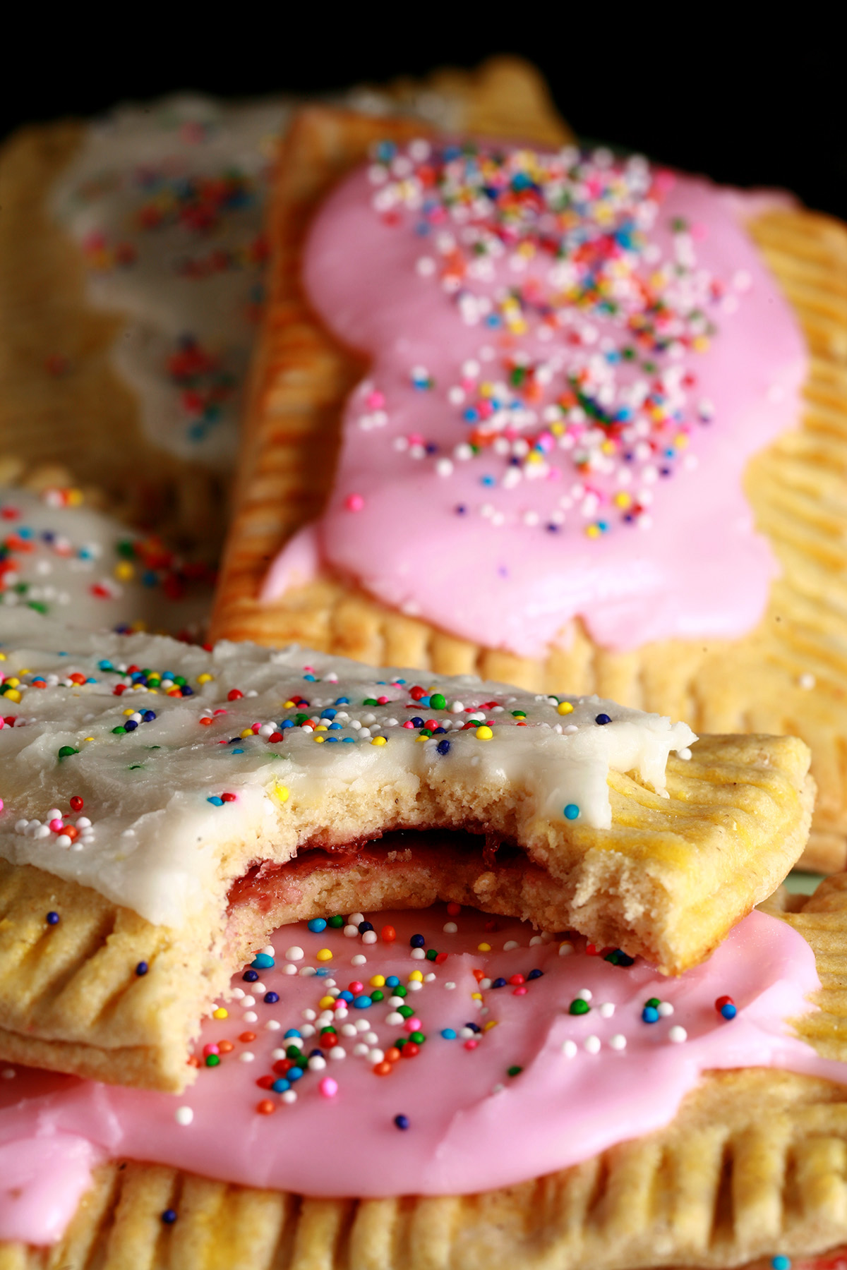 A plate of homemade gluten-free pop tarts, frosted with pink and white icing, topped with coloured sprinkles.