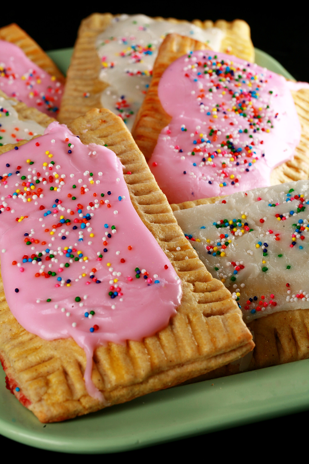 A plate of toaster pastries made from this gluten-free poptarts recipe. They are frosted with pink and white icing, and topped with coloured sprinkles.