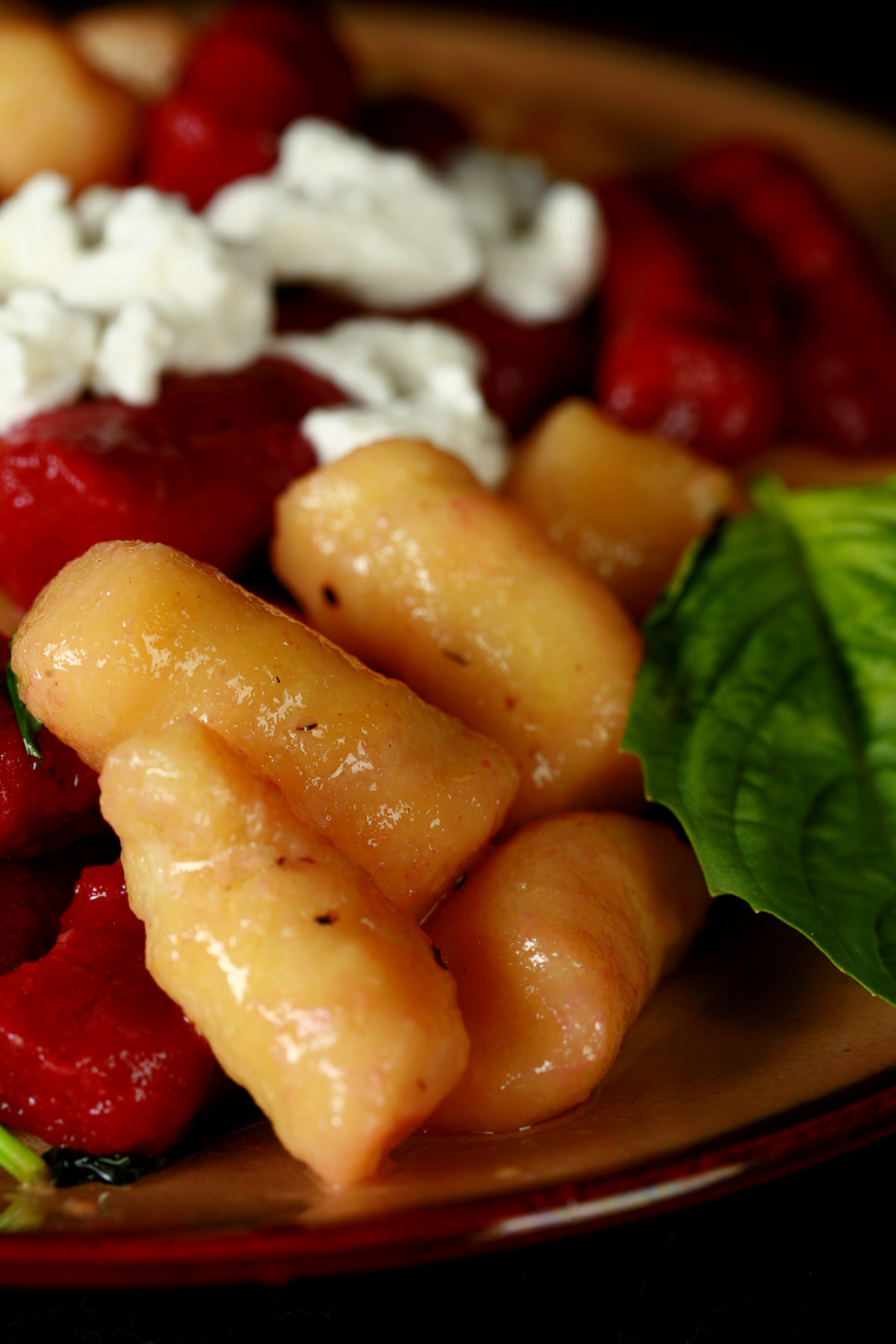 A plate of red and yellow roasted beet gnocchi. It's topped with crumbled goat cheese and fresh basil.