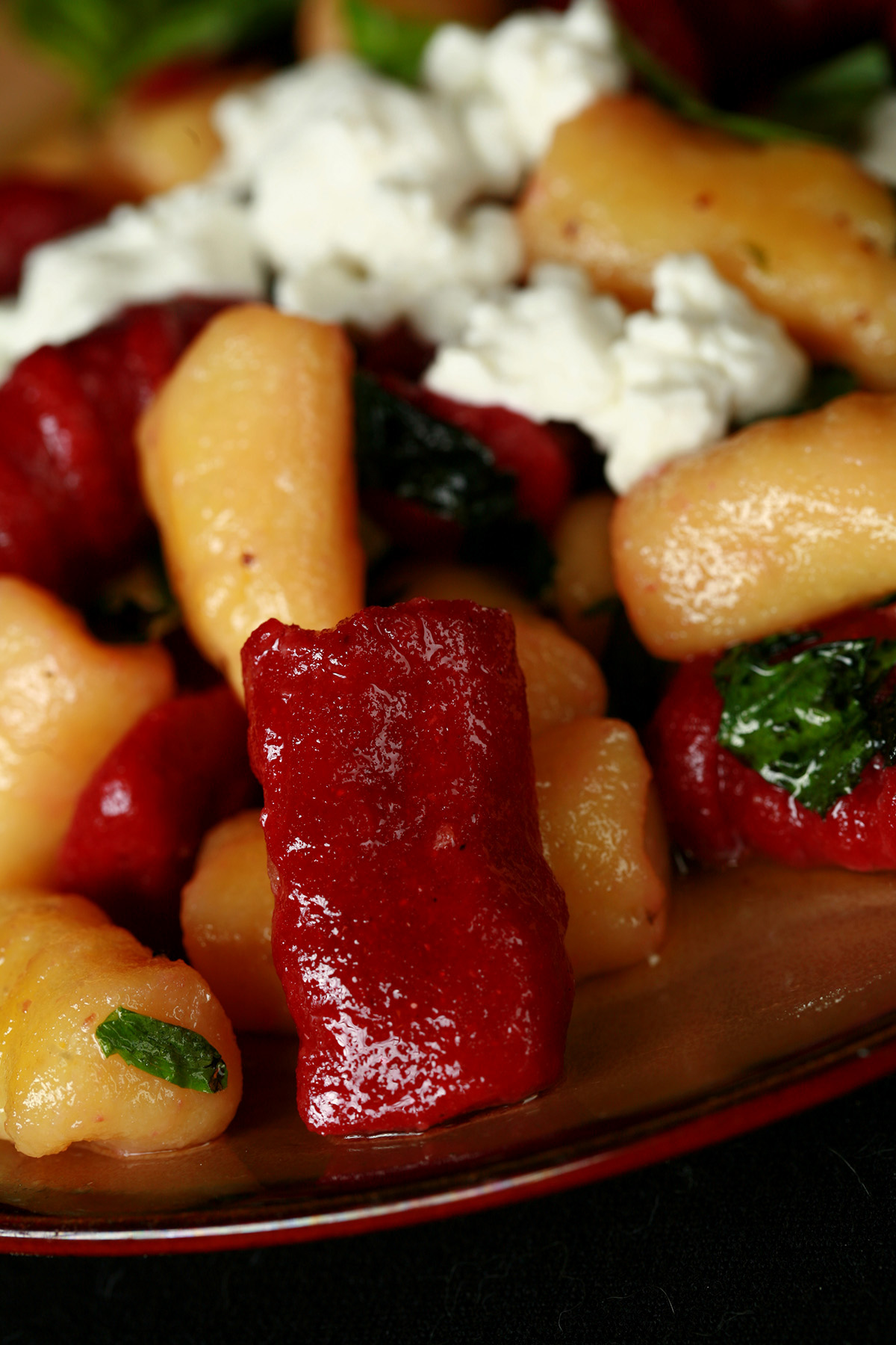 A plate of red and yellow roasted beet gnocchi. It's topped with crumbled goat cheese and fresh basil.