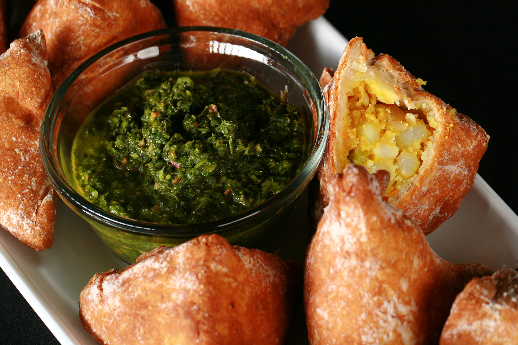 Several Gluten-Free Samosa on a tray, surrounding a small bowl of cilantro chutney.
