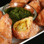 Several Gluten-Free Samosa on a tray, surrounding a small bowl of cilantro chutney.