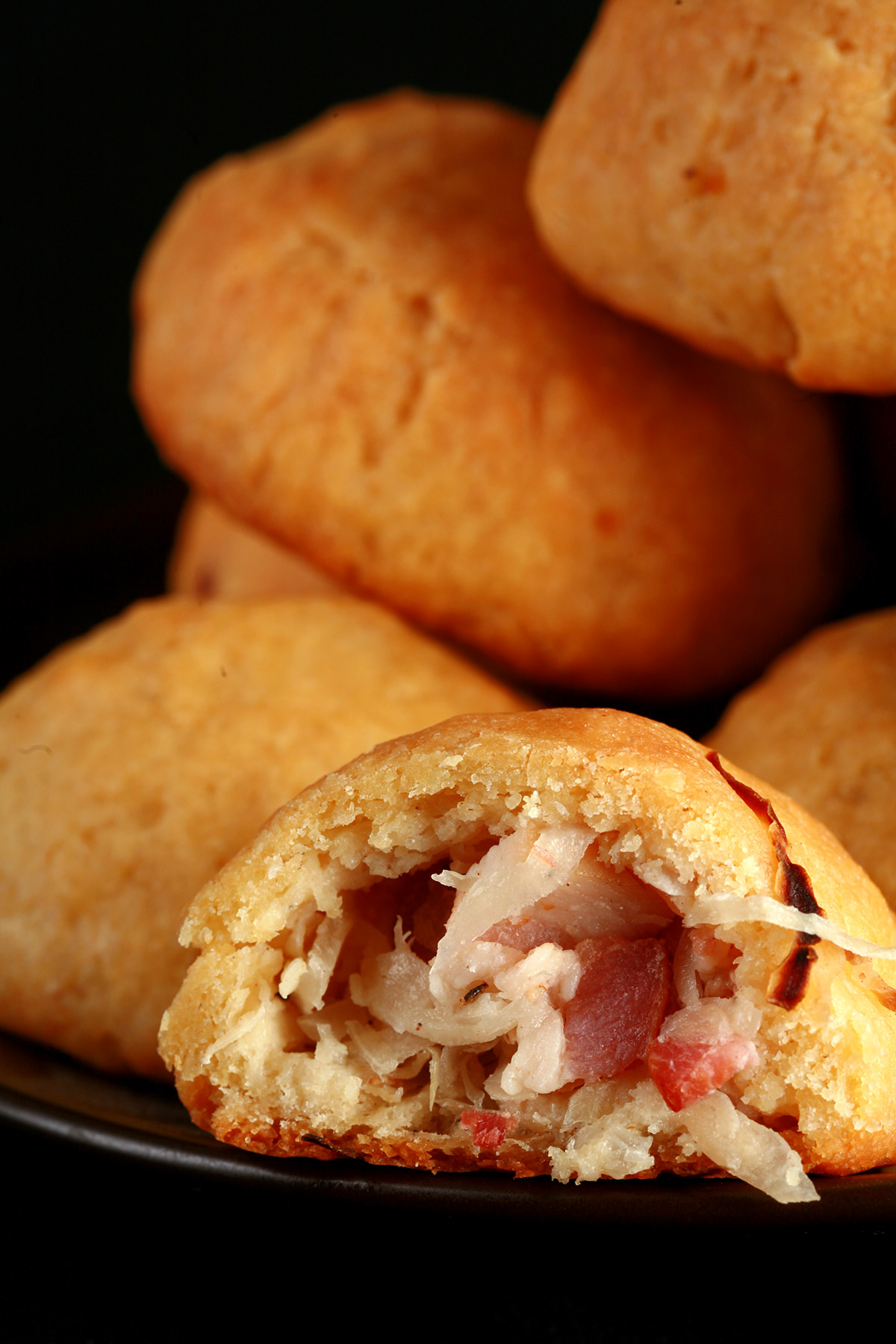 A pile of gluten-free sauerkraut balls on a small plate. One is broken in half, showing the bacon and onion mixture inside.