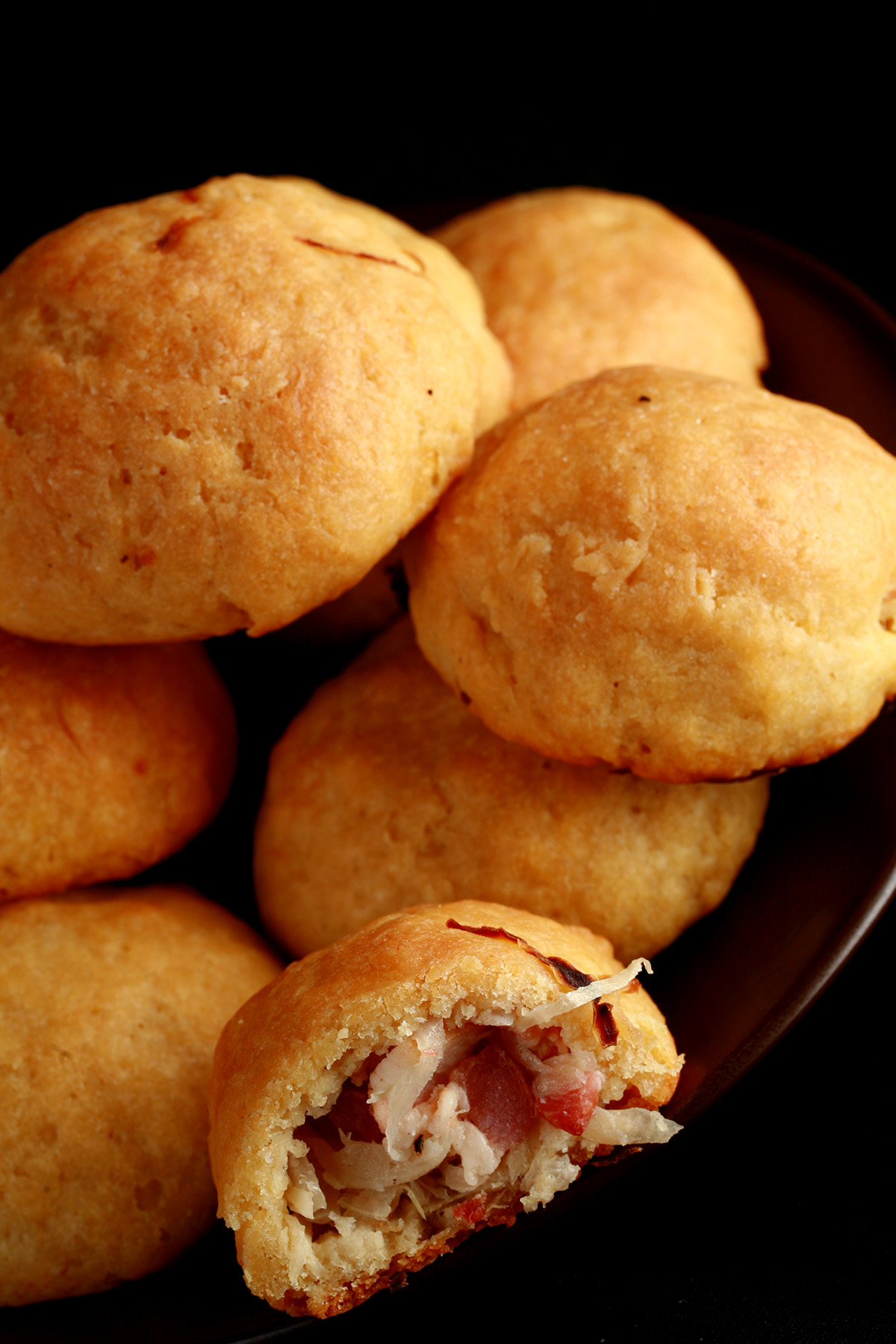 A pile of gluten-free Pyrizhky on a small plate. One is broken in half, showing the bacon and onion mixture inside.