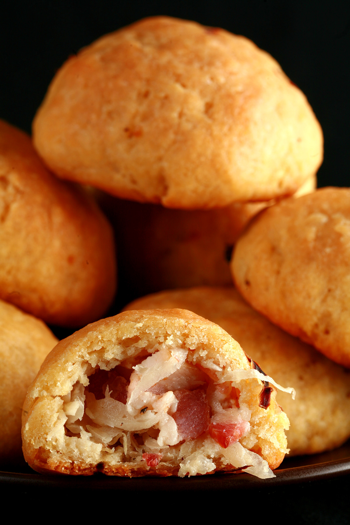 A pile of gluten-free sauerkraut balls on a small plate. One is broken in half, showing the bacon and onion mixture inside.