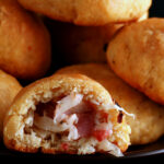 A pile of gluten-free Pyrizhky on a small plate. One is broken in half, showing the bacon and onion mixture inside.