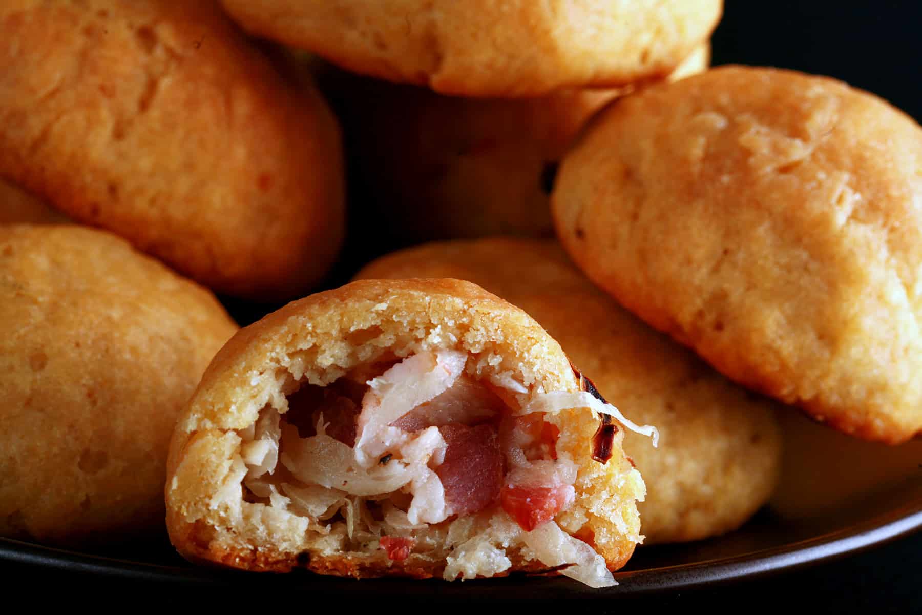 A pile of gluten-free Pyrizhky on a small plate. One is broken in half, showing the bacon and onion mixture inside.