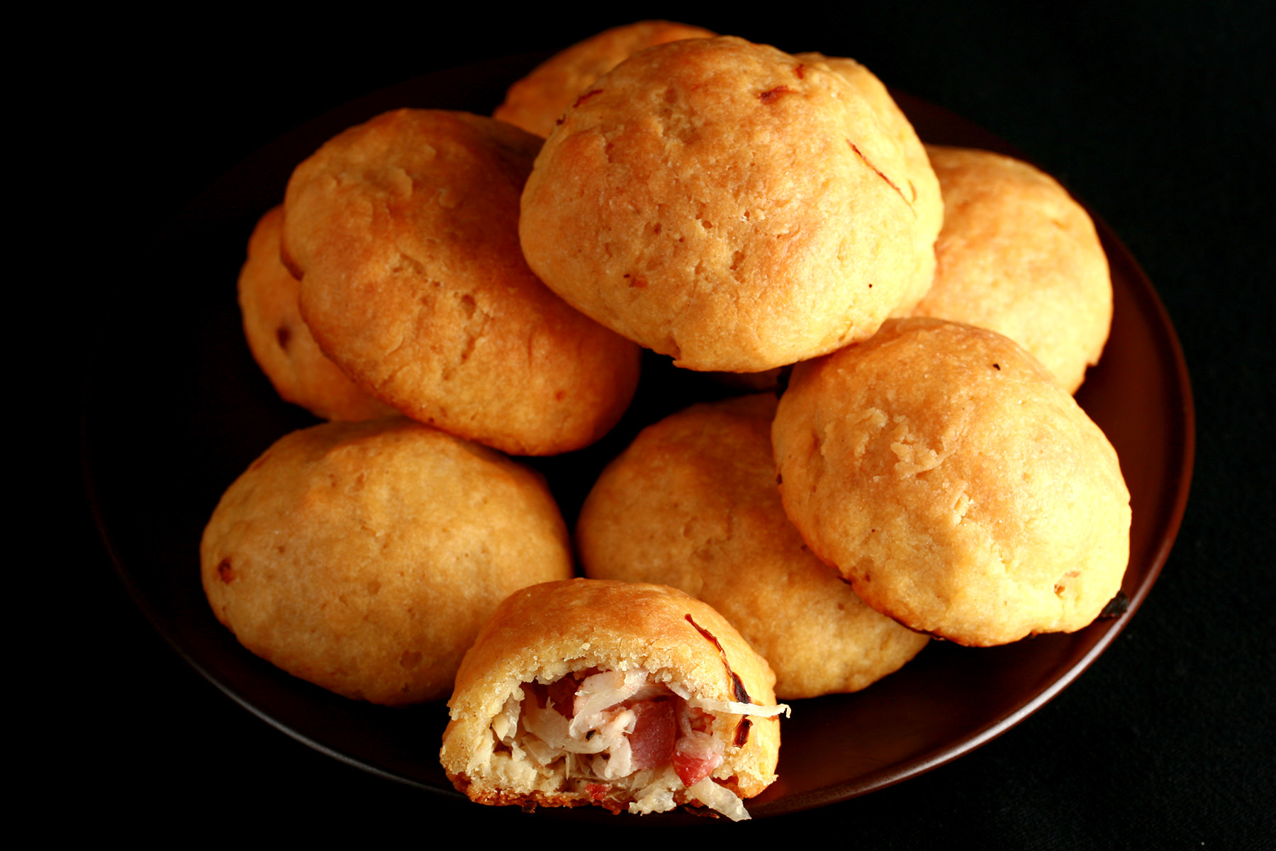 A pile of gluten-free sauerkraut balls on a small plate. One is broken in half, showing the bacon and onion mixture inside.