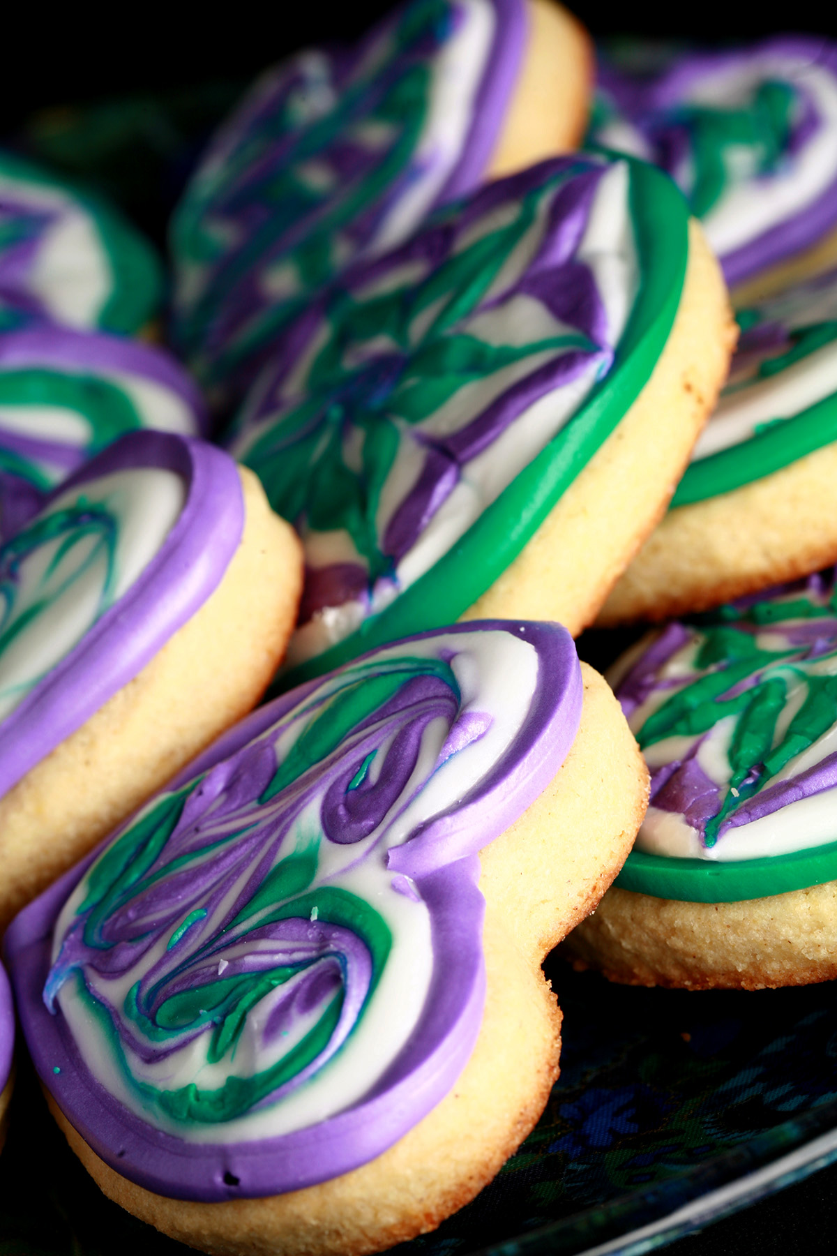 Close up view of a plate of heart shaped cookies decorated with swirls of teal and lavender over white.