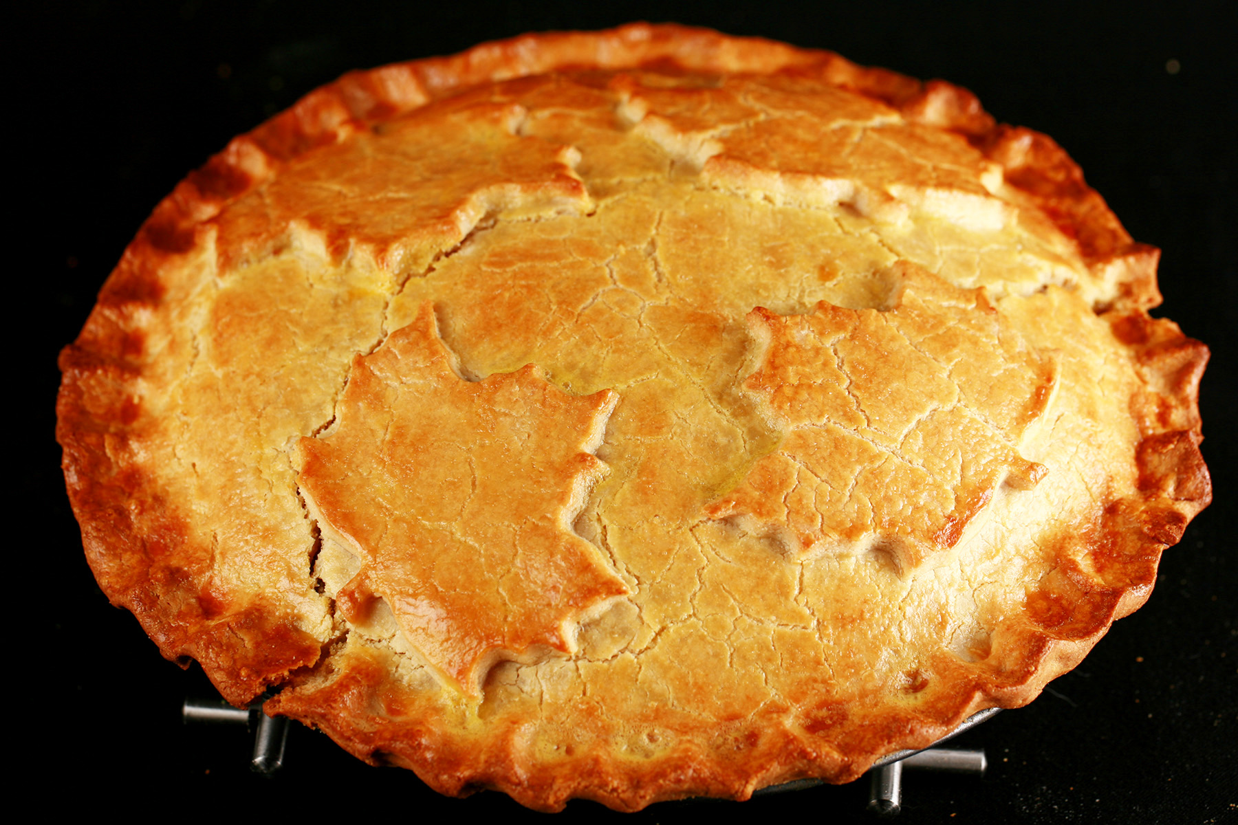 A golden brown gluten-free tourtiere meat pie, with a maple leaf design on top.