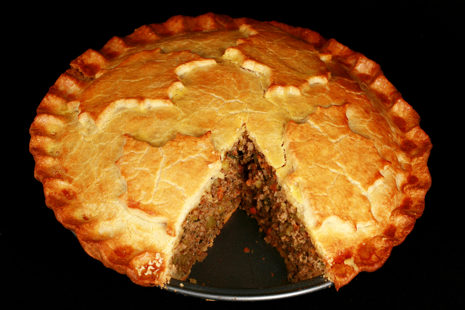 A golden brown gluten-free tourtiere meat pie, with a maple leaf design on top.. There is a section cut out of it