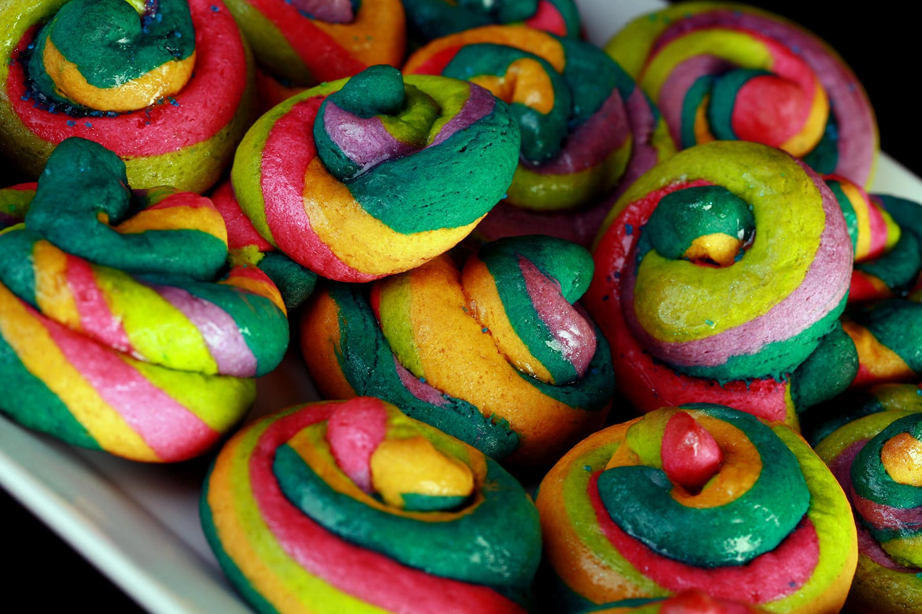 A close up view of a pile of gluten-free unicorn poop cookies. They are brightly coloured cookie "poops" made from brightly coloured twists of cookie dough.