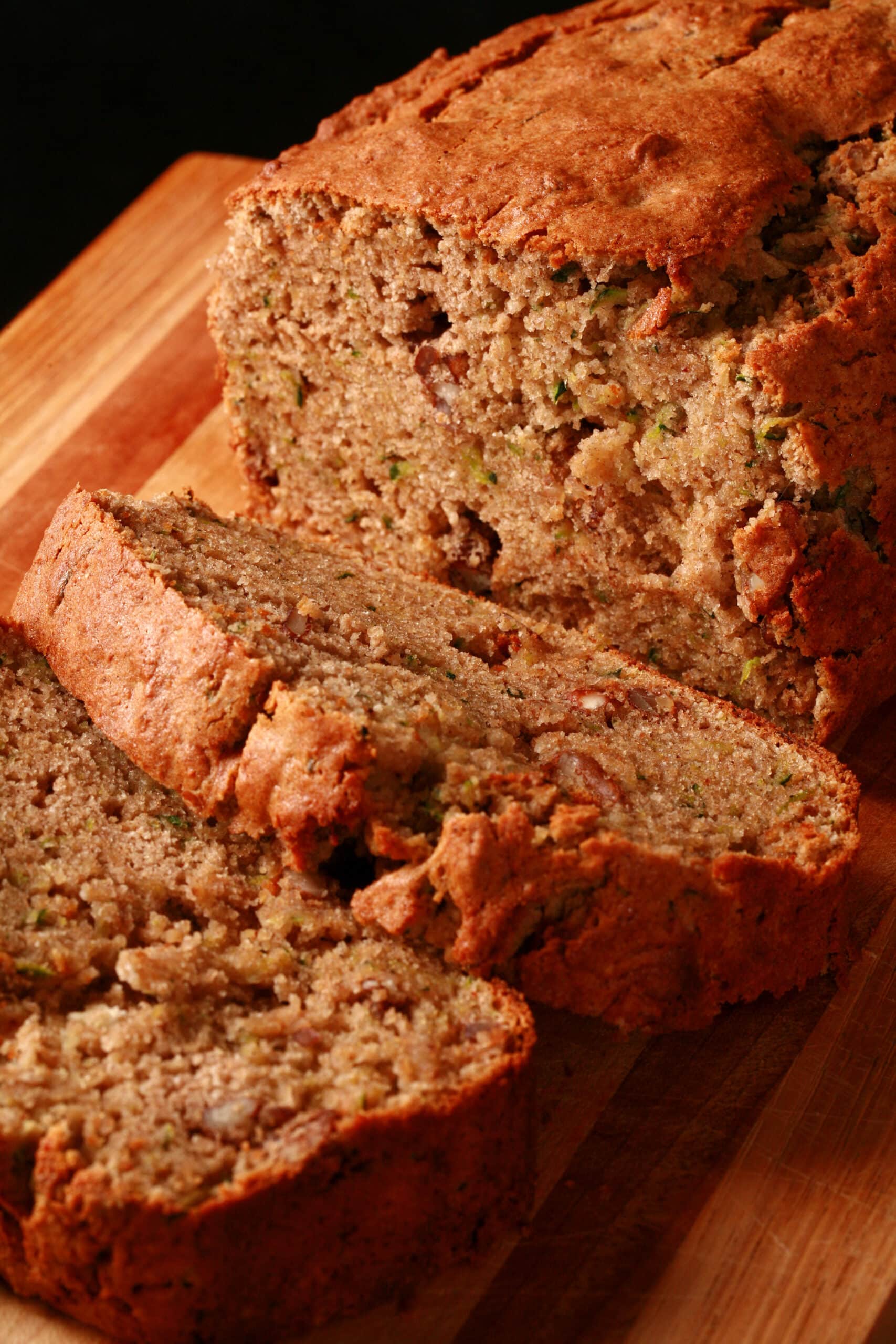 A sliced loaf of gluten free zucchini bread on a wooden cutting board.