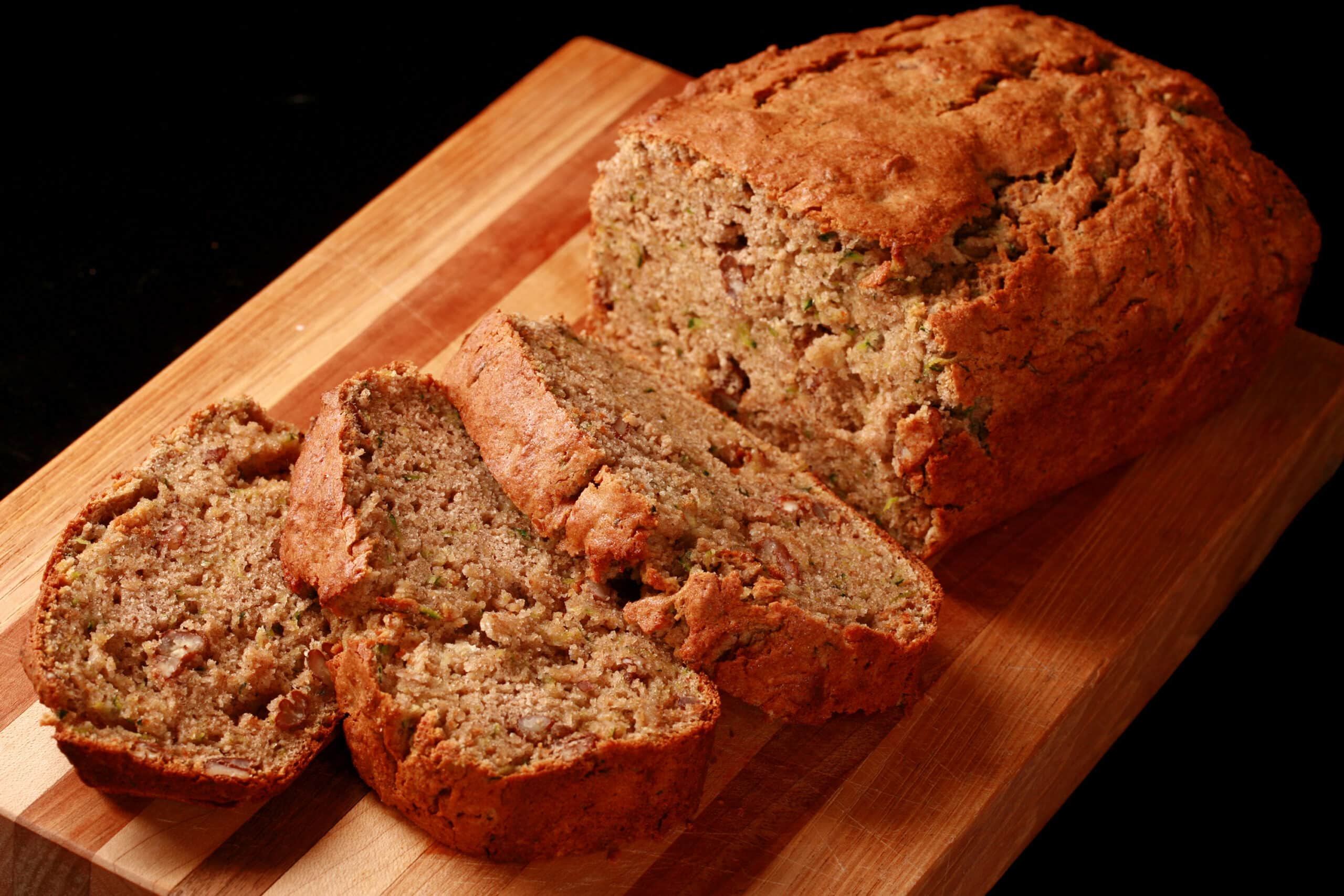 A sliced loaf of gluten free zucchini bread on a wooden cutting board.