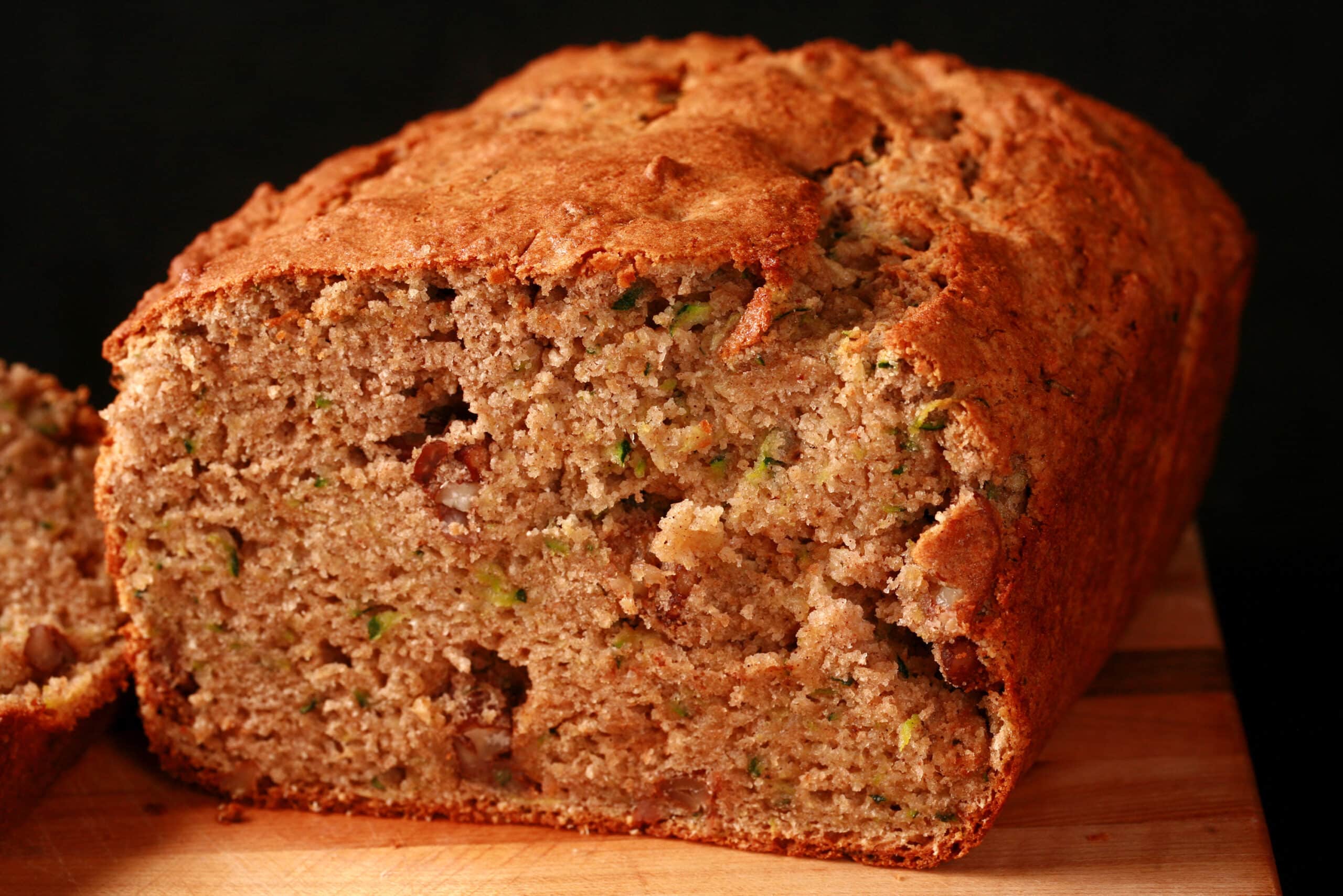 A sliced loaf of gluten-free zucchini bread on a wooden cutting board.