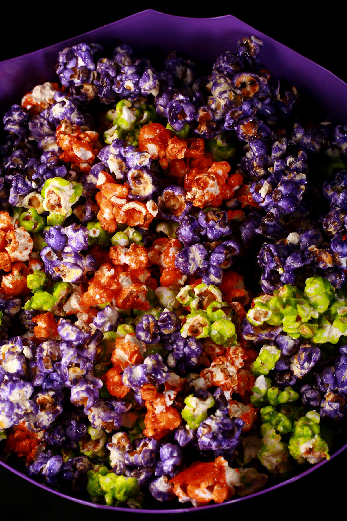 A bowl of Halloween popcorn - orange, purple, and lime green glazed popcorn, mixed together.