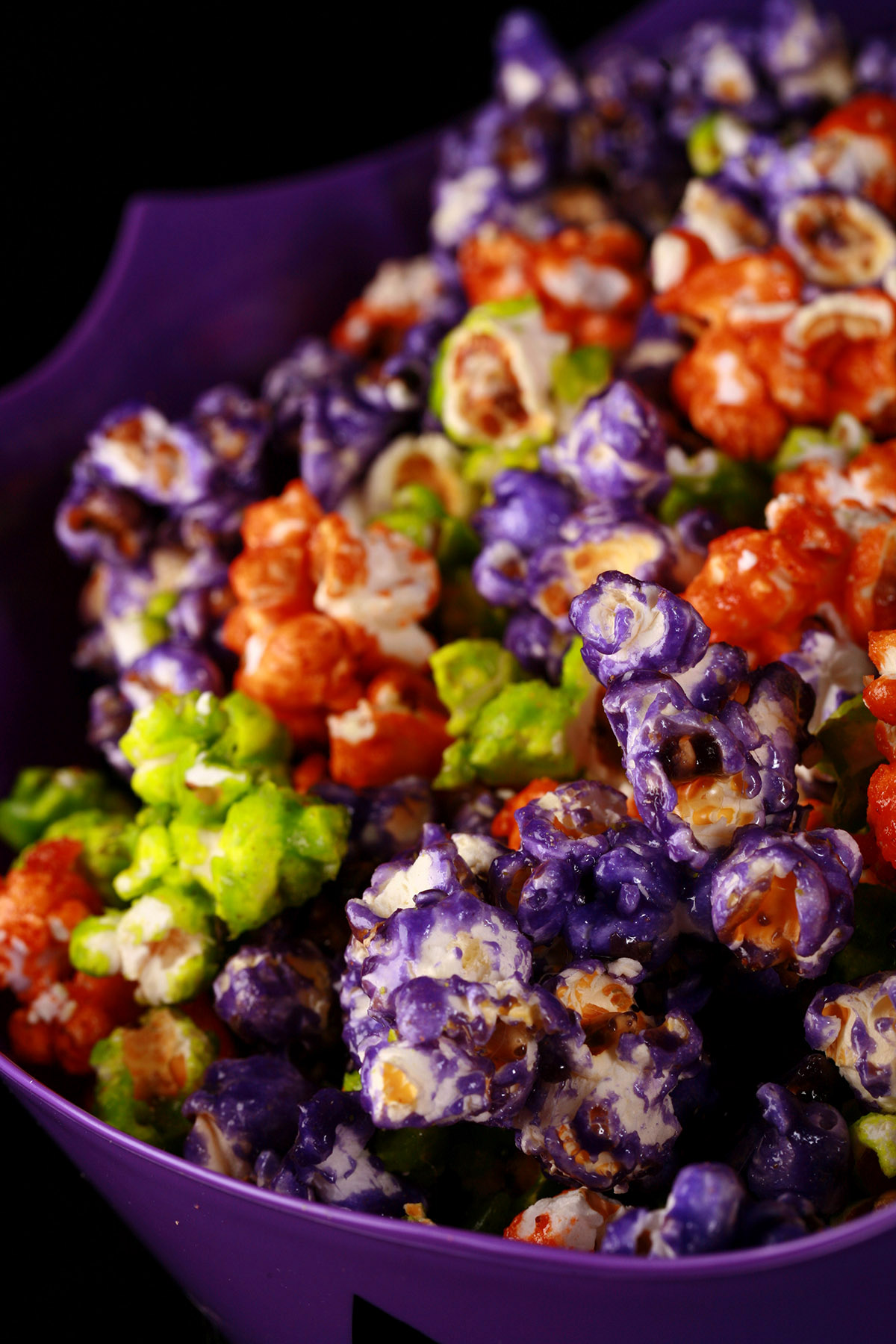 A bowl of Halloween glazed popcorn - orange, purple, and lime green mixed together.