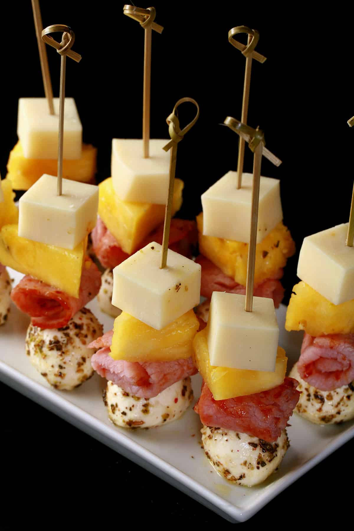 A tray of hawaiian pizza themed ham and pineapple skewers.