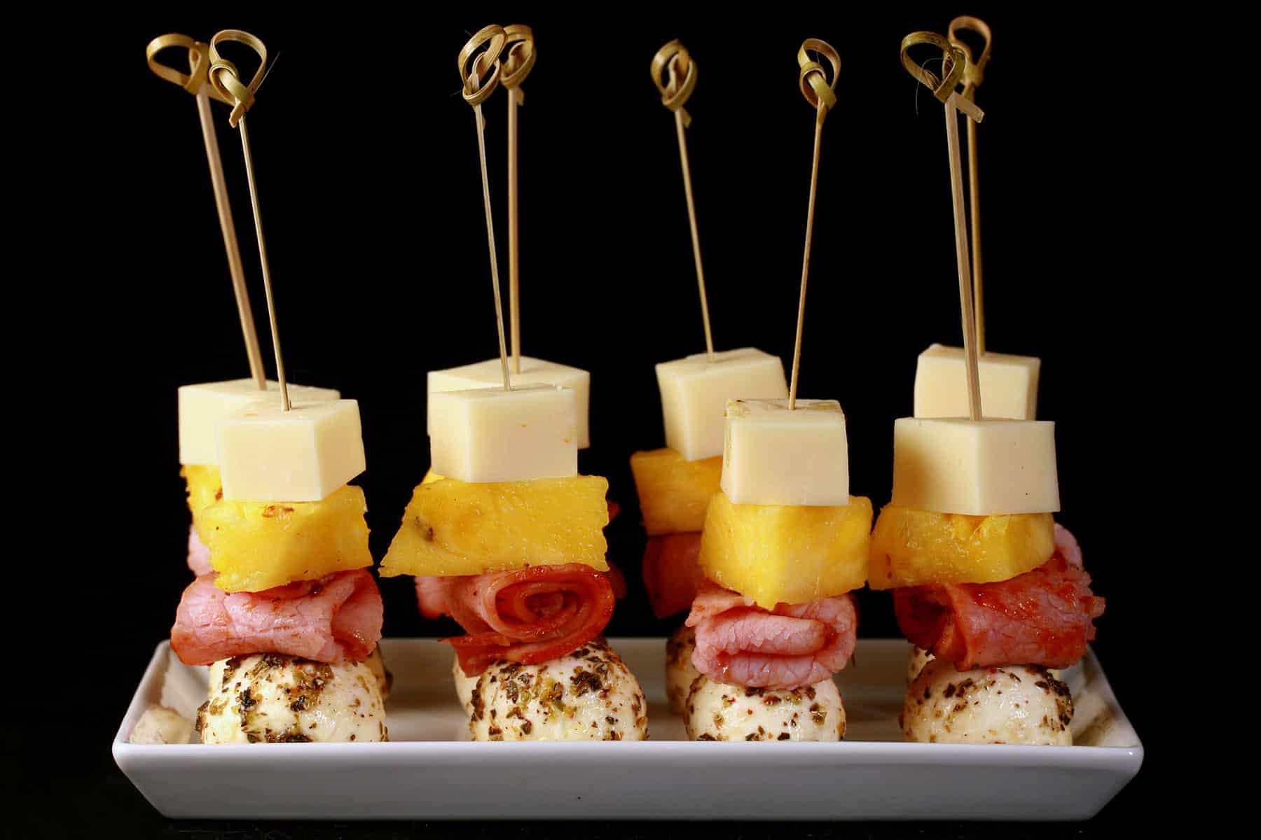 A tray of hawaiian pizza skewers - pineapple, back bacon, and 2 kinds of cheese.