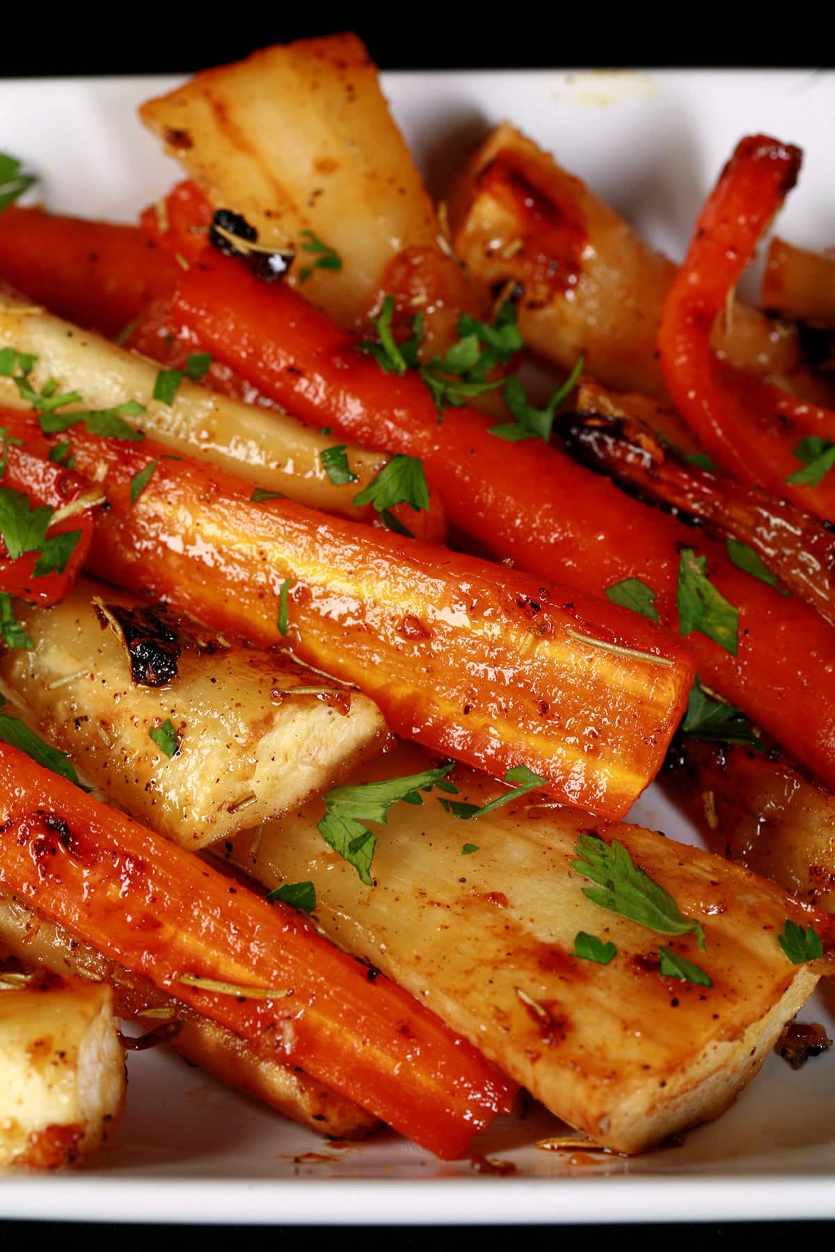 A platter of honey roasted carrots and parsnips, sprinkled with parsley.