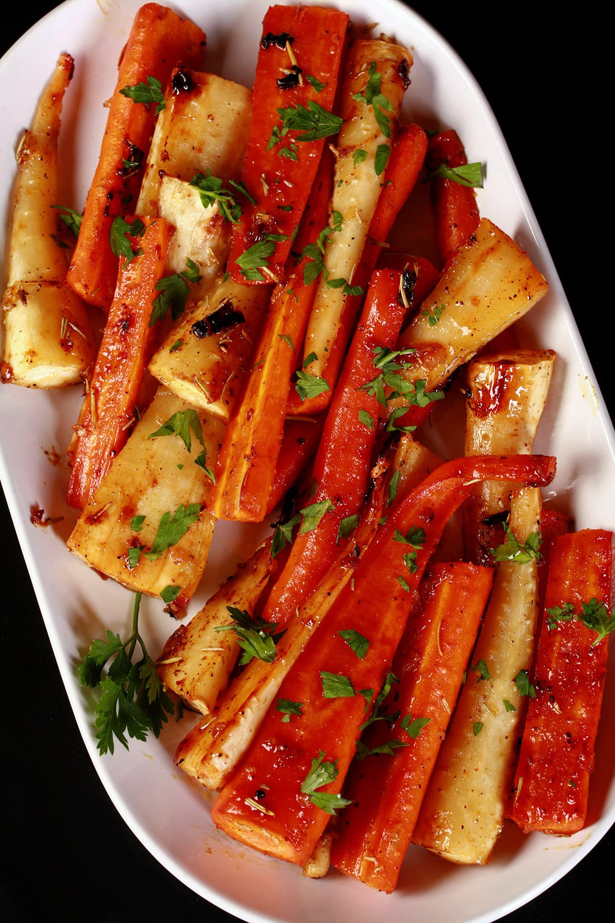A platter of honey roasted carrots and parsnips, sprinkled with parsley.