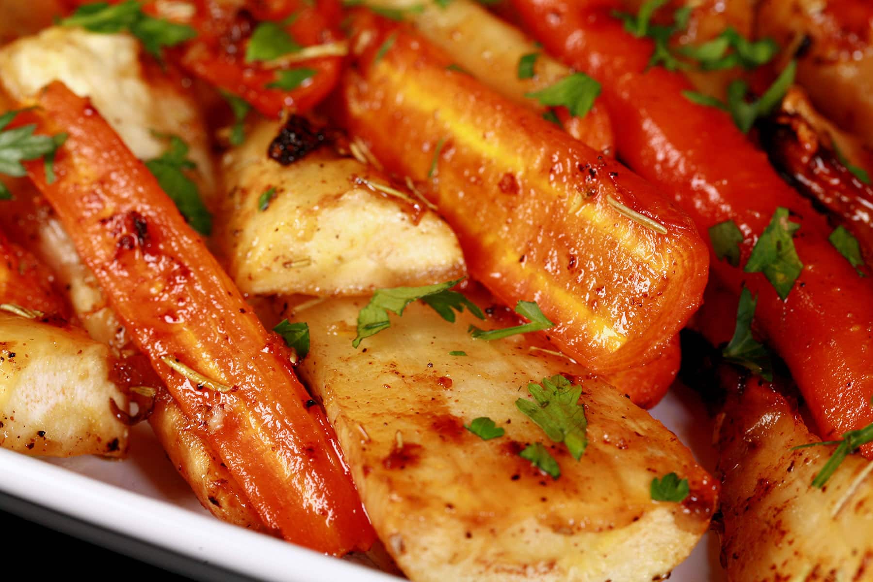 A platter of honey roasted parsnips and carrots, sprinkled with parsley.