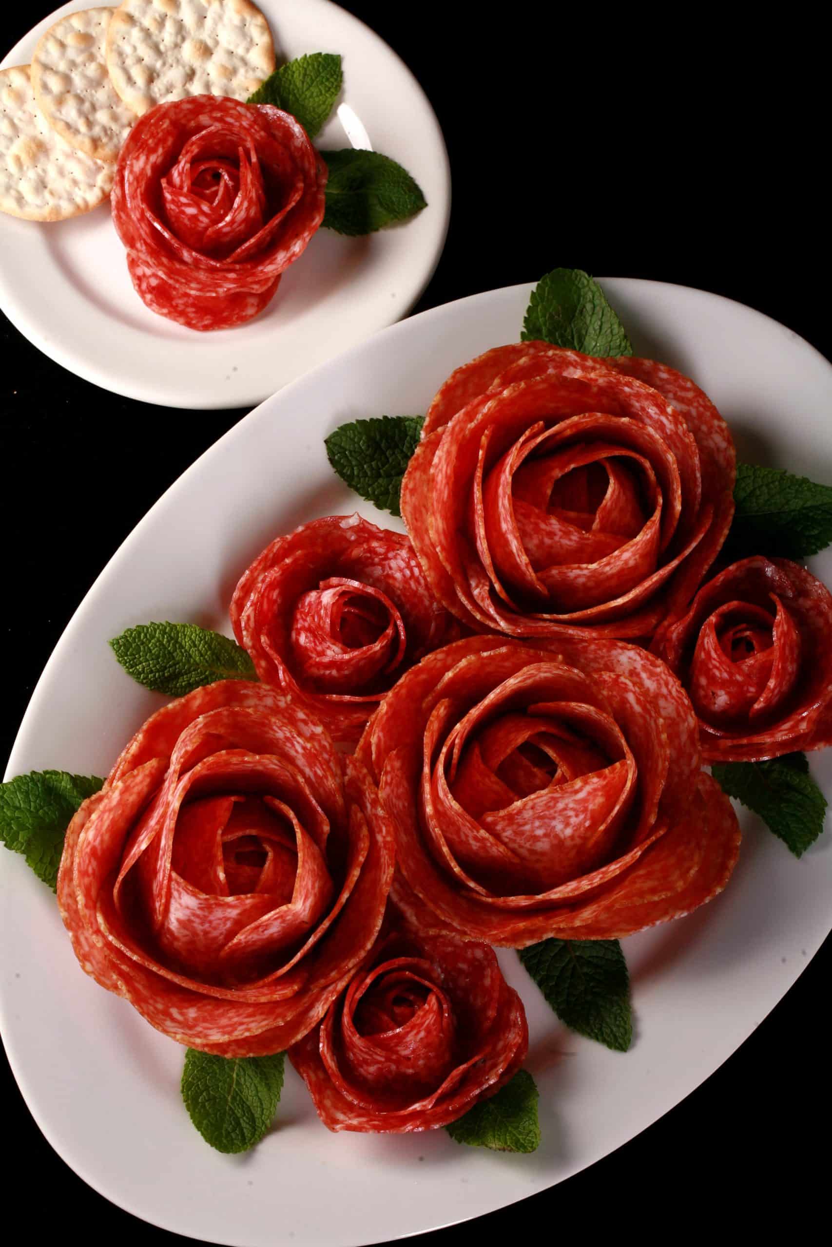 A plate of large and small charcuterie roses, accented with mint leaves.