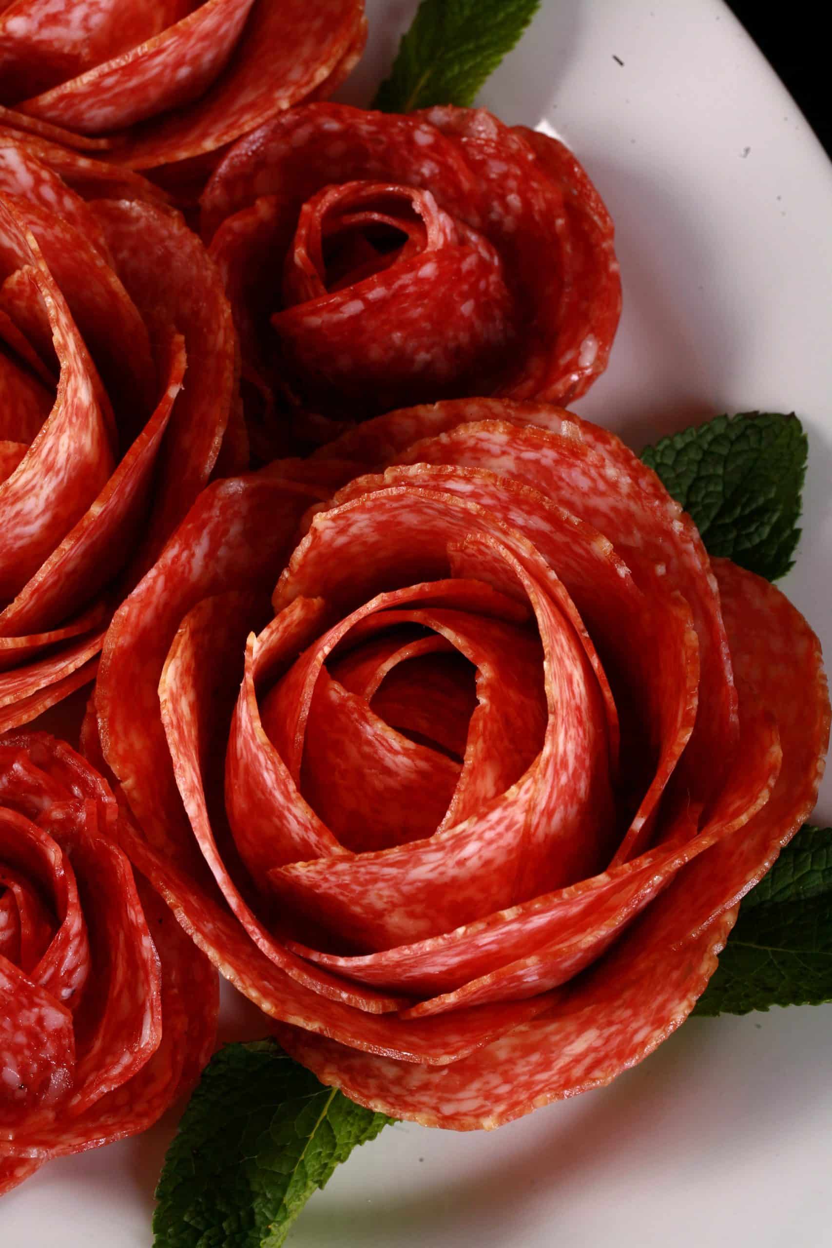 A plate of large and small salami roses, accented with mint leaves.