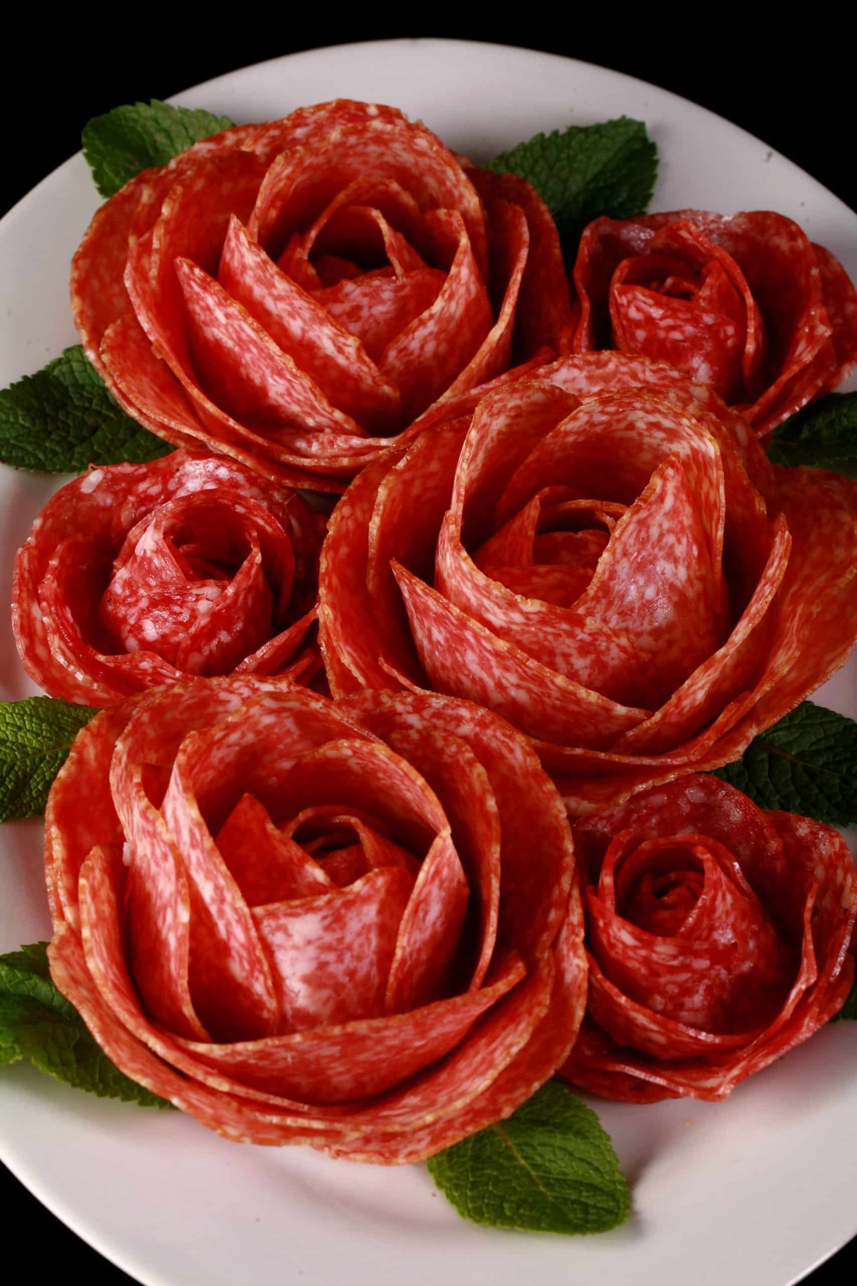 A plate of large and small charcuterie roses, accented with mint leaves.