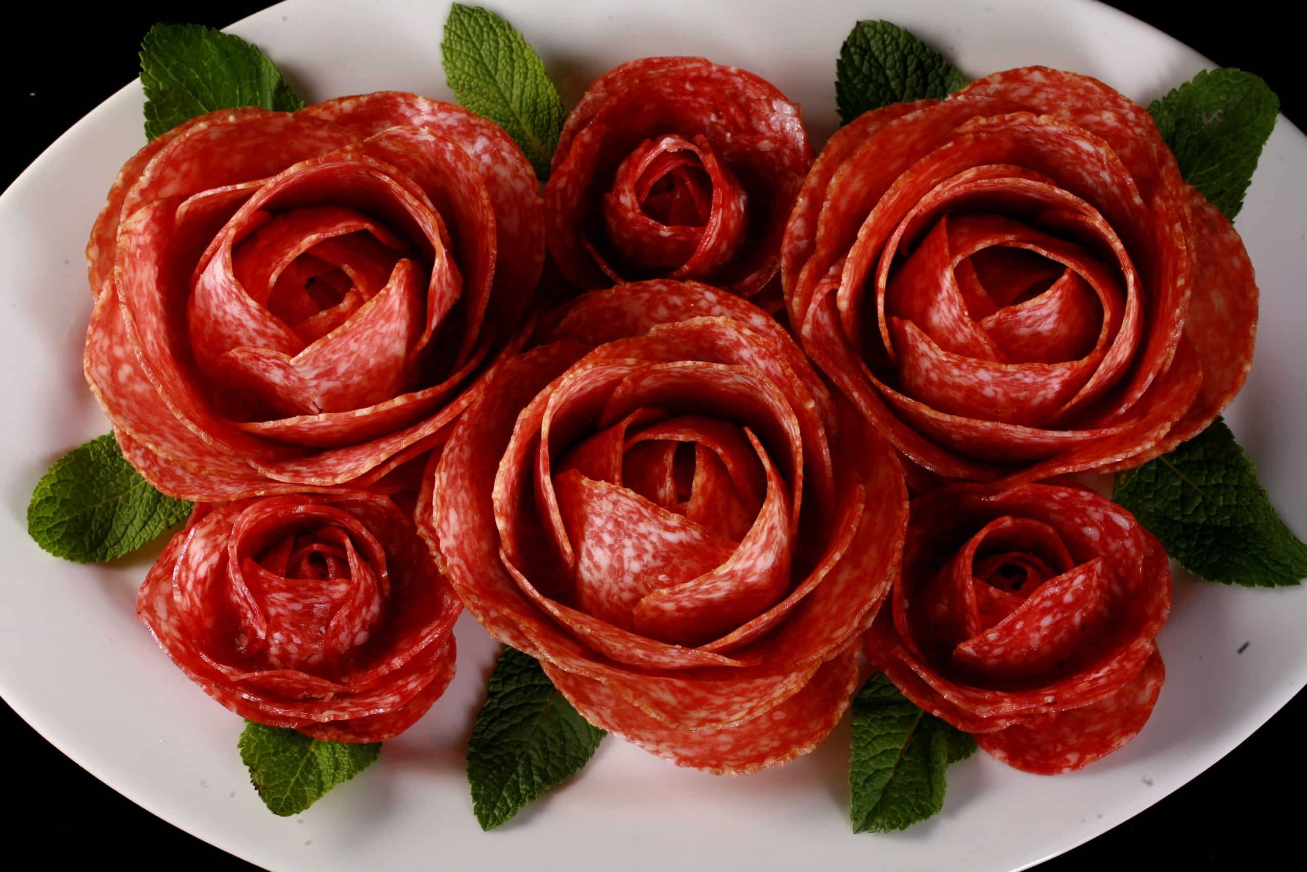 A plate of large and small salami roses, accented with mint leaves.