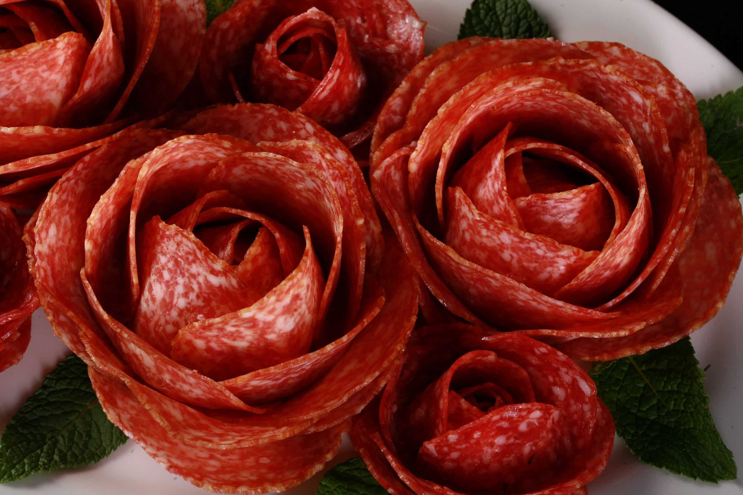 A plate of large and small charcuterie roses, accented with mint leaves.