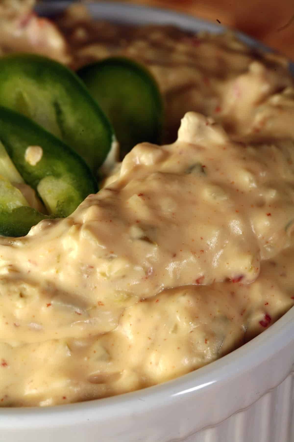 A ramekin of bacon jalapeno dip, surrounded by corn chips and topped with sliced jalapenos.