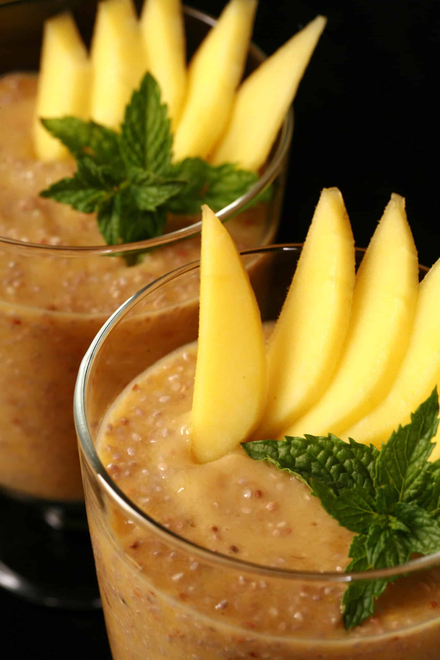 2 glasses of mango chia pudding, garnished with mango slices and fresh mint leaves.