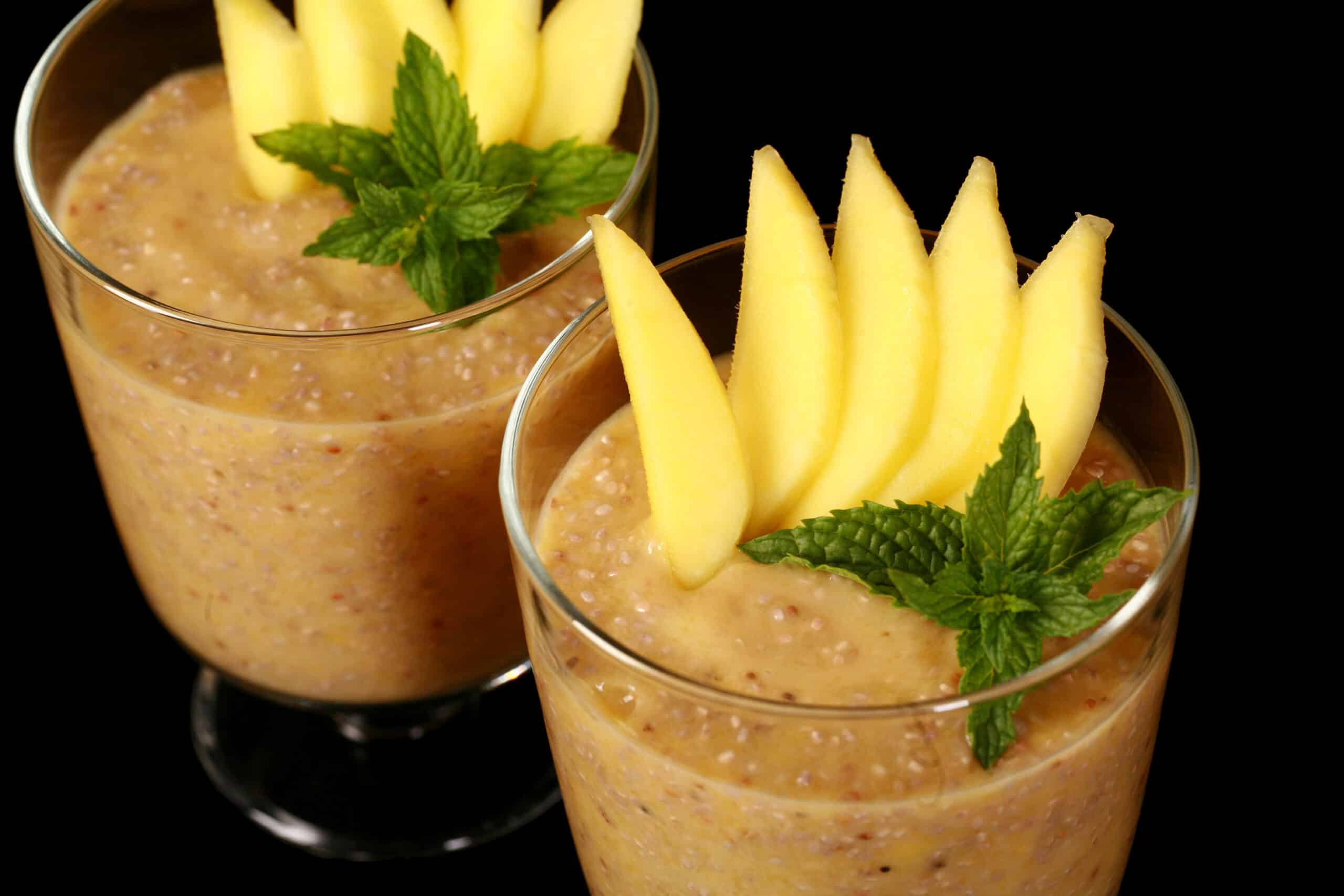 2 glasses of mango chia pudding, garnished with mango slices and fresh mint leaves.