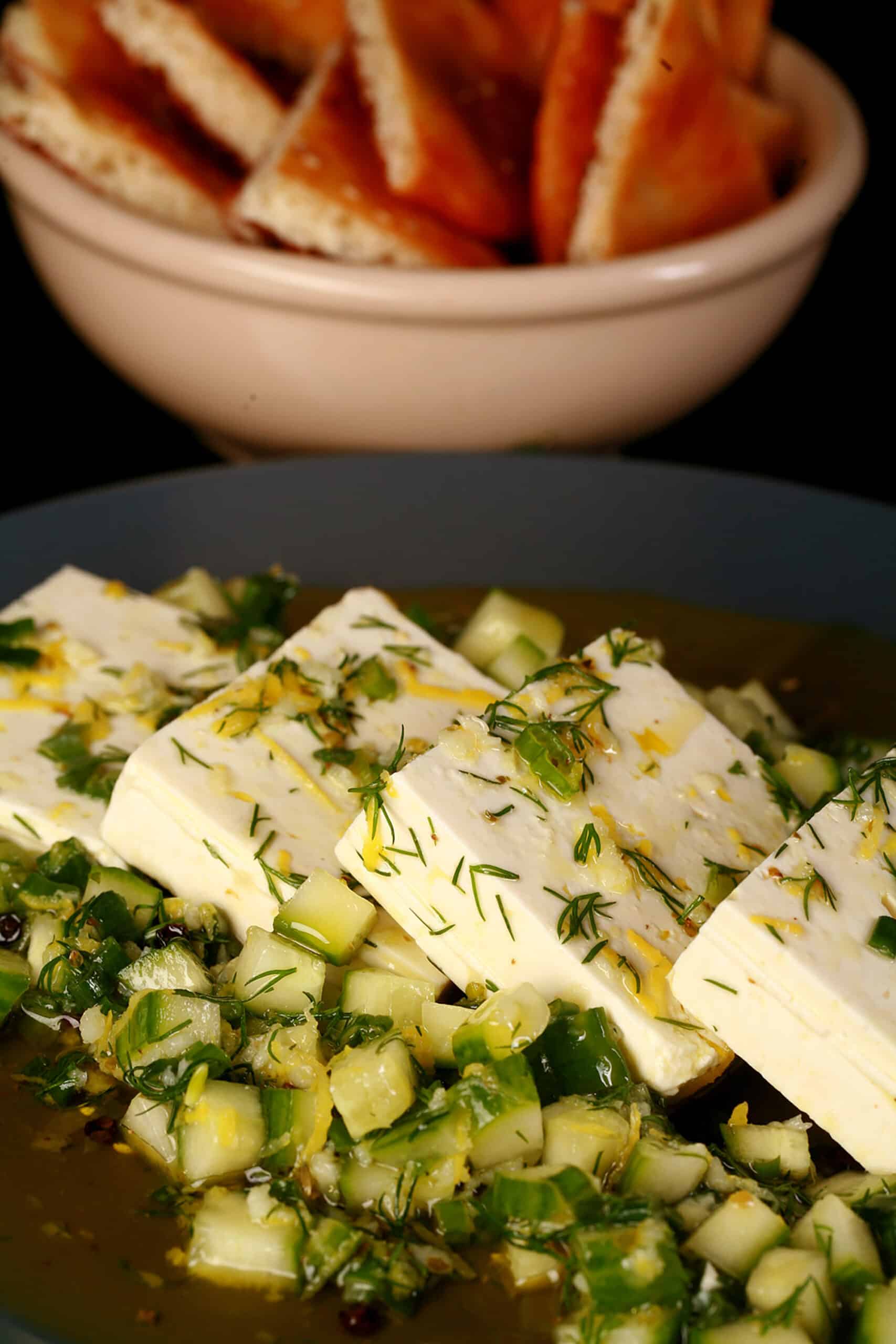 4 slices of lemon herb marinated feta cheese on a bed of marinated cucumber.