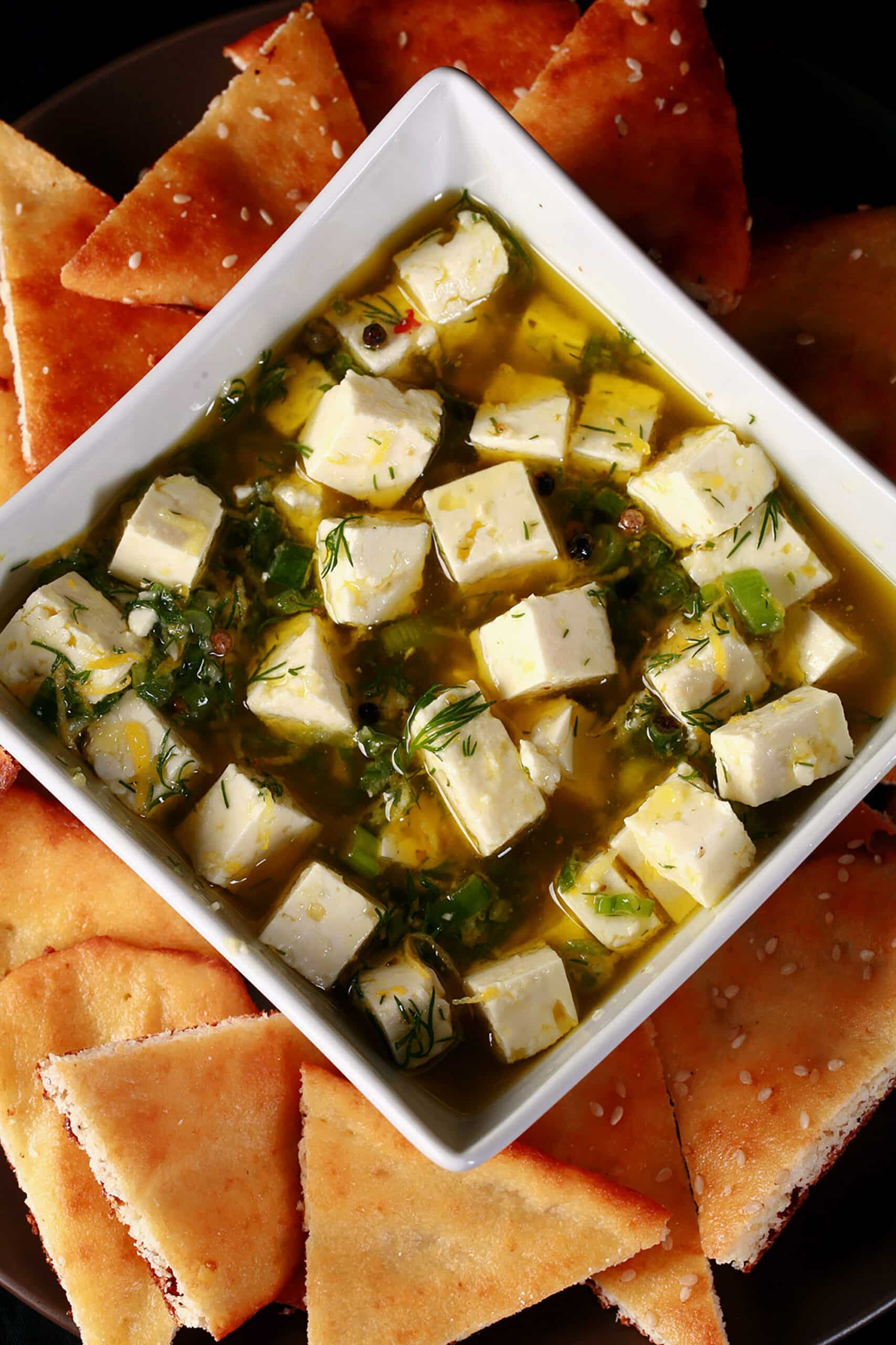 A bowl of lemon herb marinated feta surrounded with gluten free flatbread.