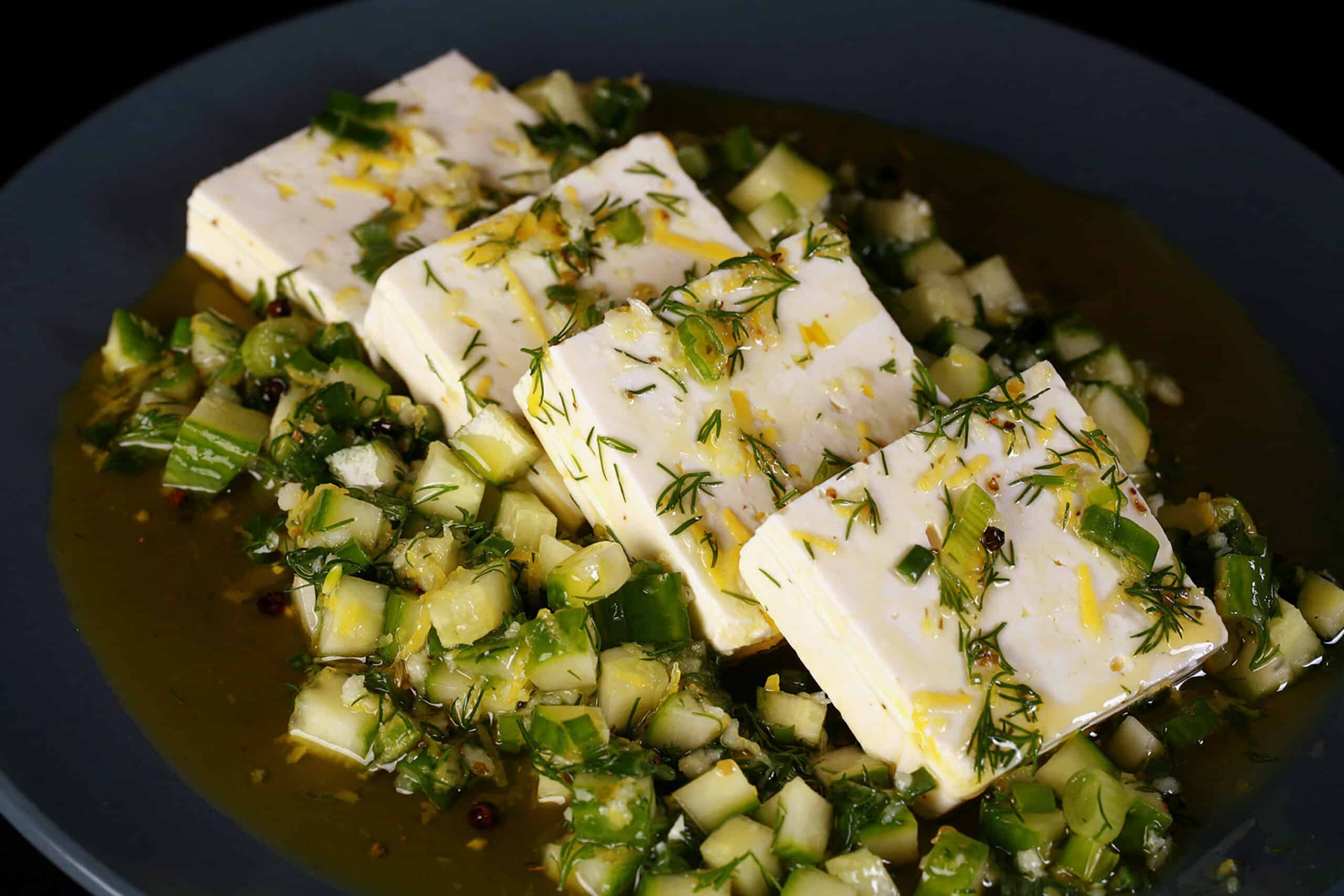 4 slices of lemon herb marinated feta cheese on a bed of marinated cucumber.