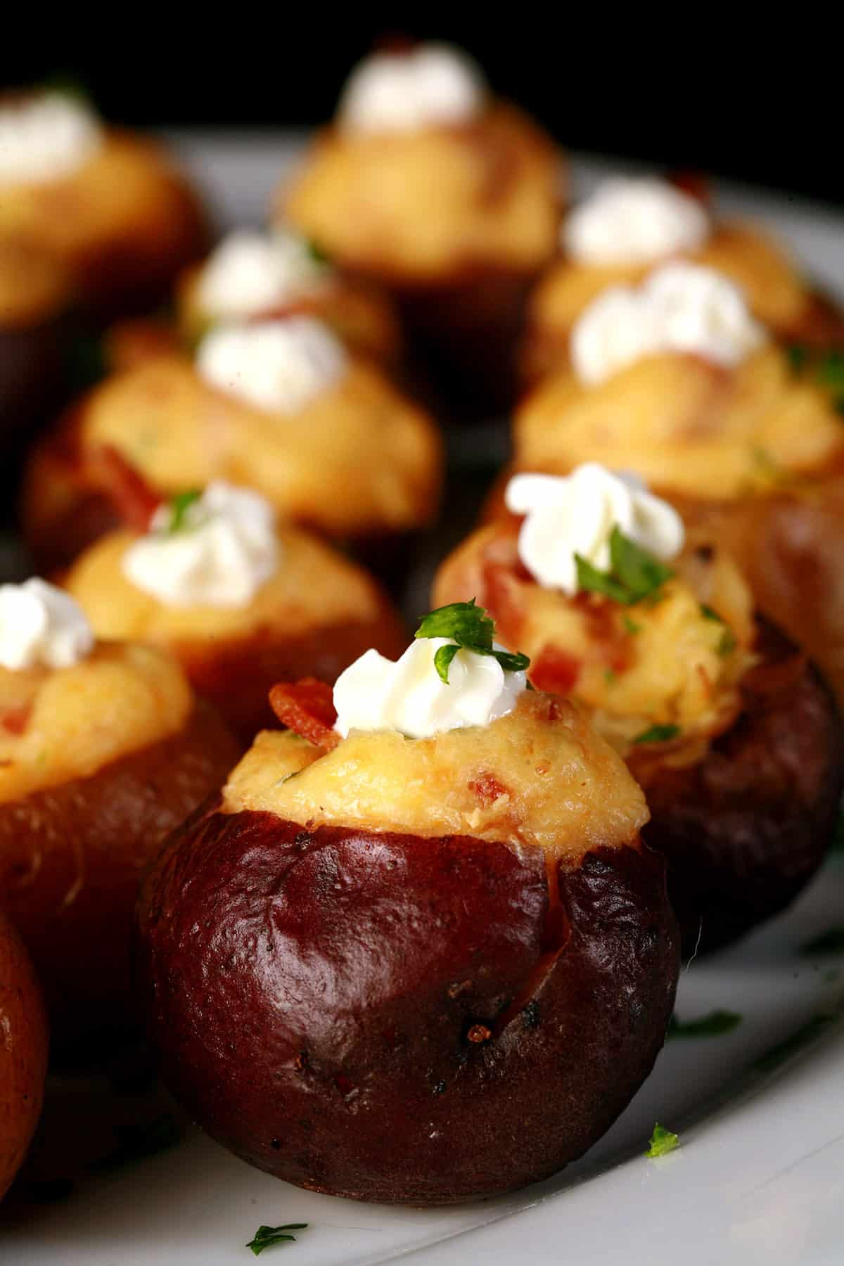 A party platter of mini loaded baked potatoes, topped with sour cream, bacon, and green onion.