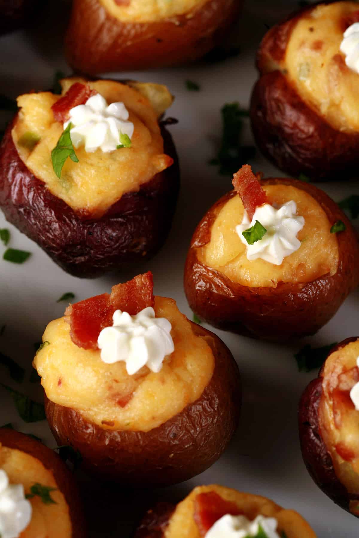 A party platter of loaded mini baked potatoes, topped with sour cream, bacon, and green onion.