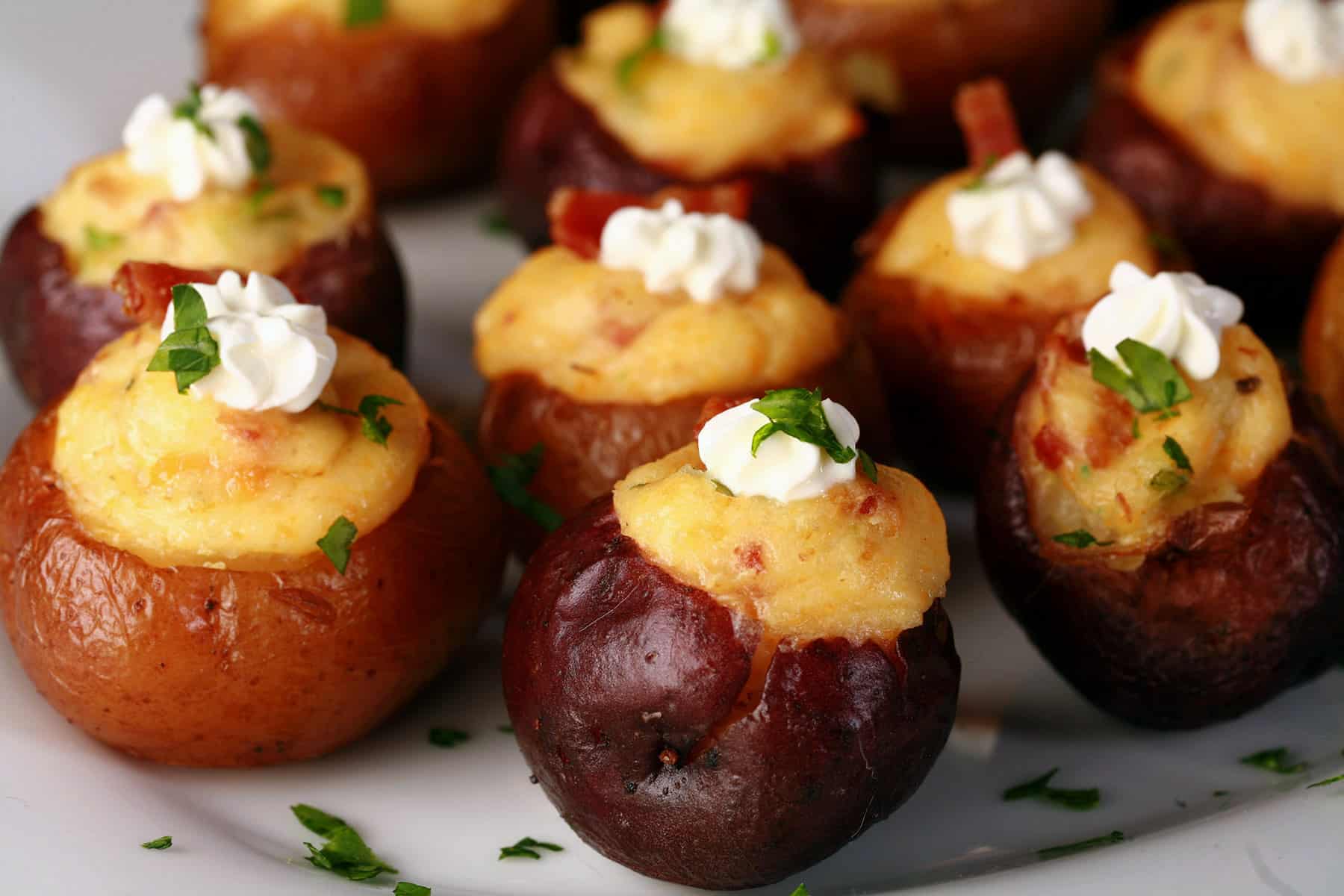 A party platter of mini loaded baked potatoes, topped with sour cream, bacon, and green onion.