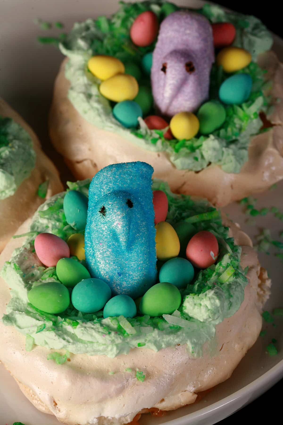A trio of Easter themed mini pavlovas. Each is topped with mini chocolate eggs and a marshmallow peep.