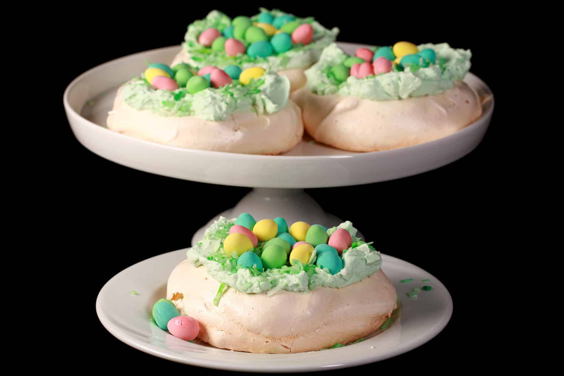 Mini easter pavlovas on a plate and a cake stand. Each have green coconut and cadbury mini eggs on top.