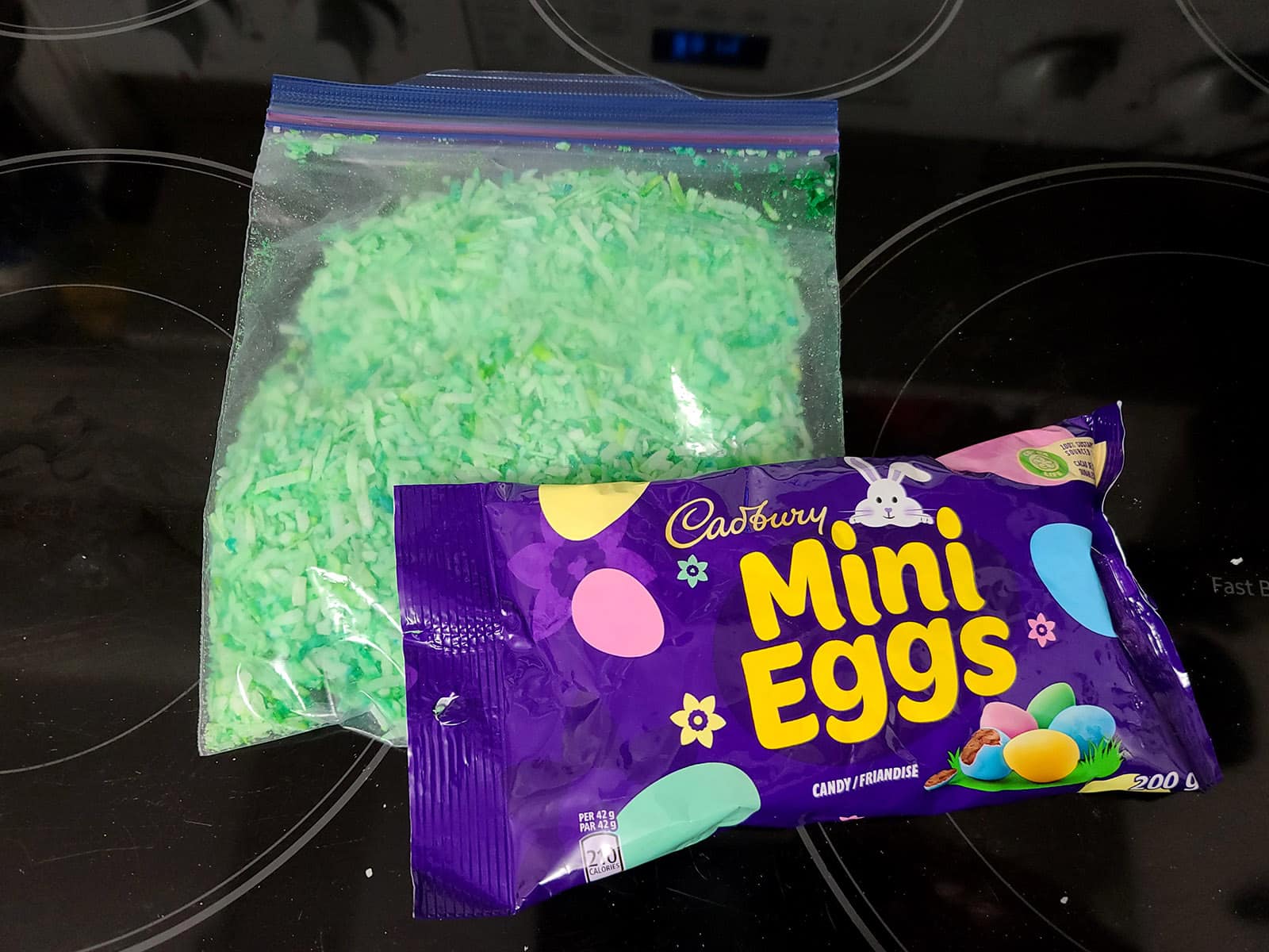 A bag of green tinted coconut and a baggie of cadbury mini eggs.
