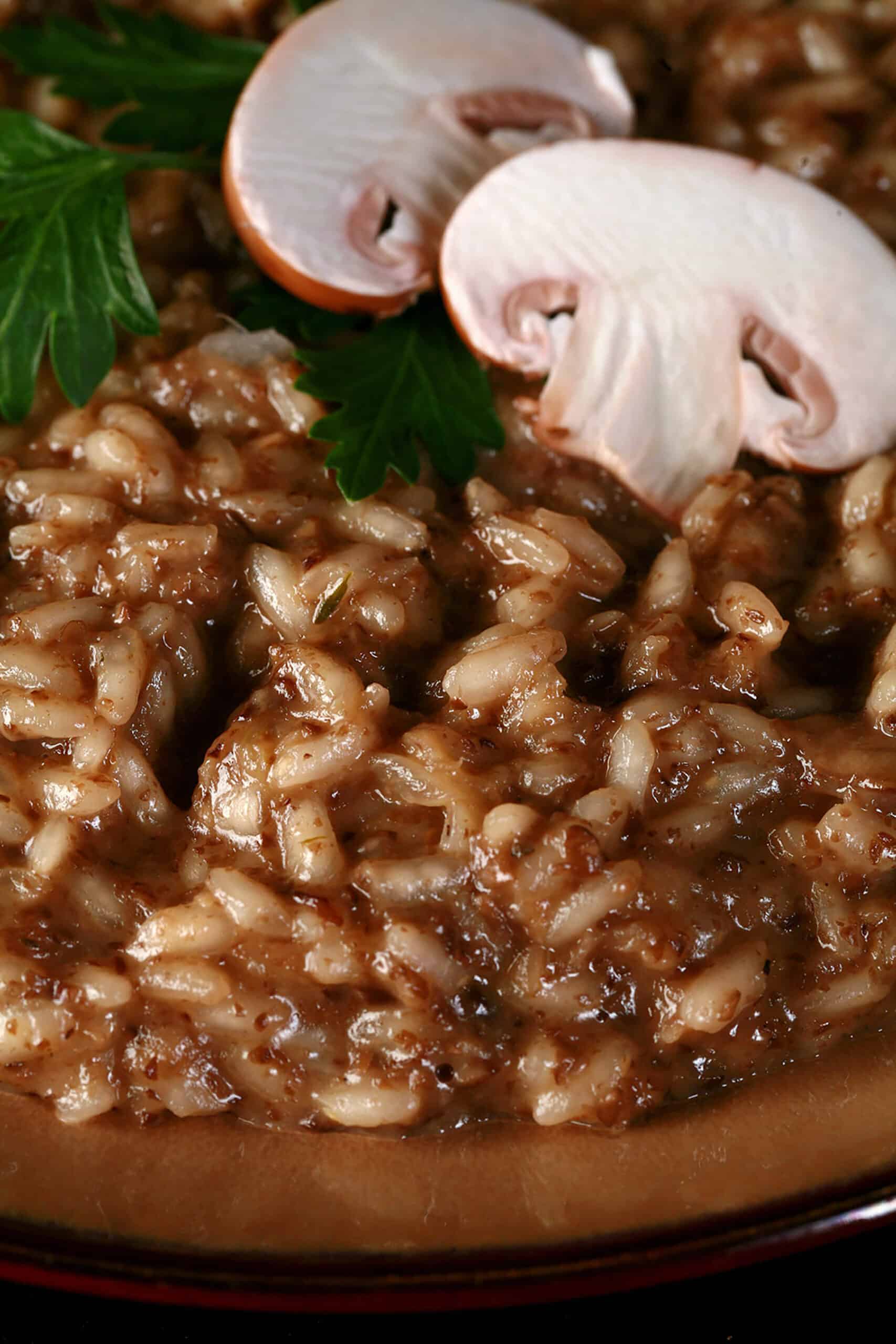 A plate of mushroom risotto, garnished with parsley leaves and sliced mushrooms.
