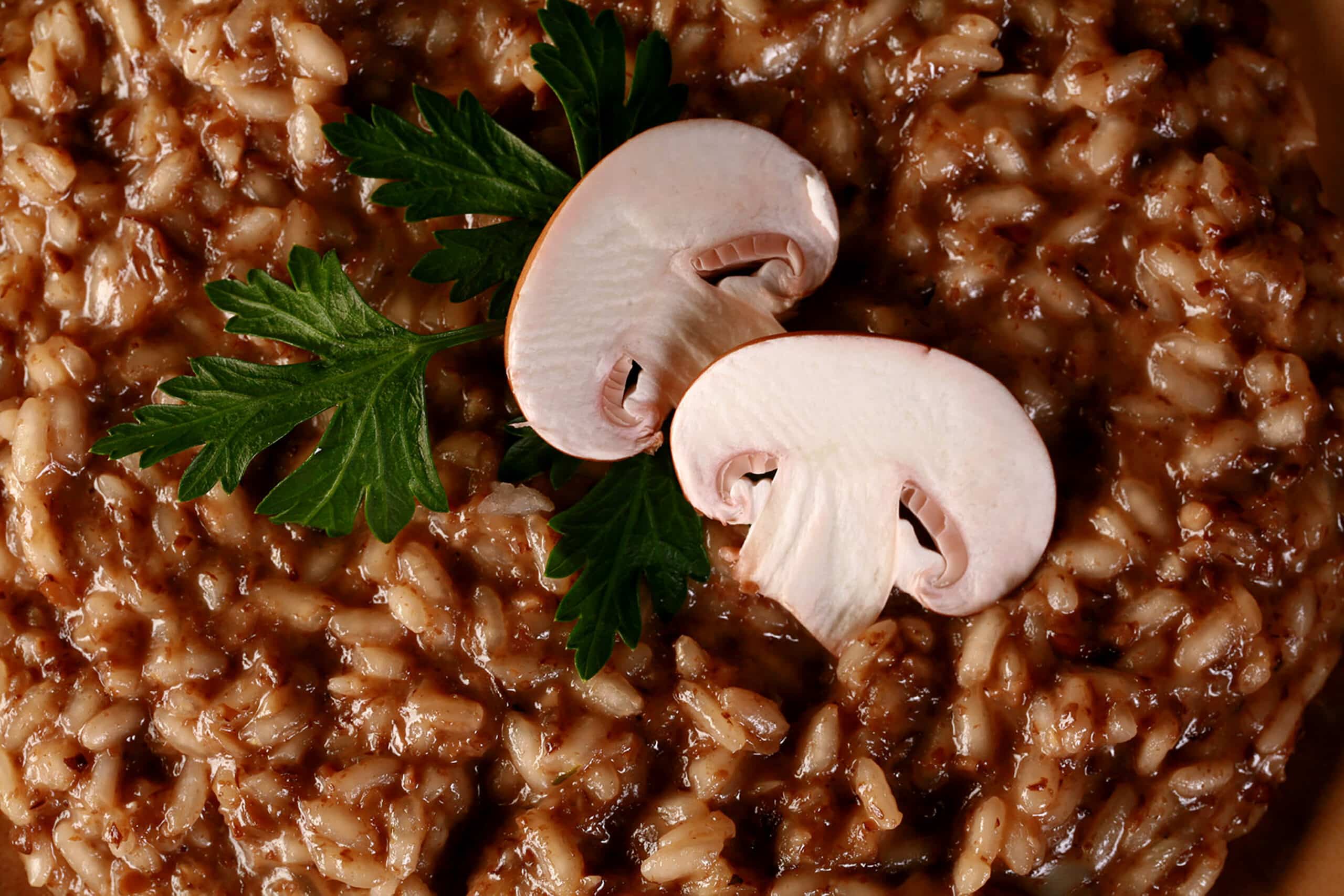 A plate of mushroom risotto, garnished with parsley leaves and sliced mushrooms.